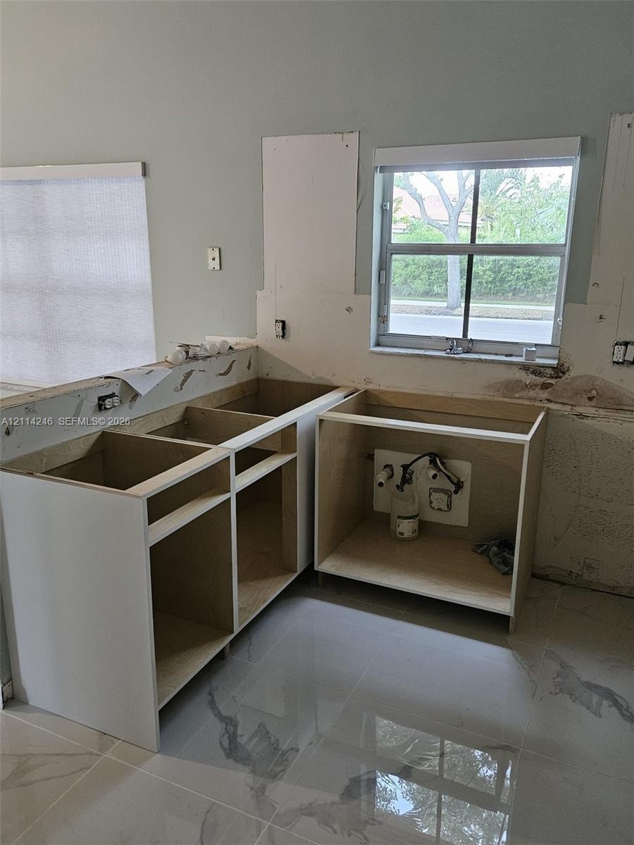 Unfinished kitchen cabinetry featuring white melamine frames and large-format polished tile flooring