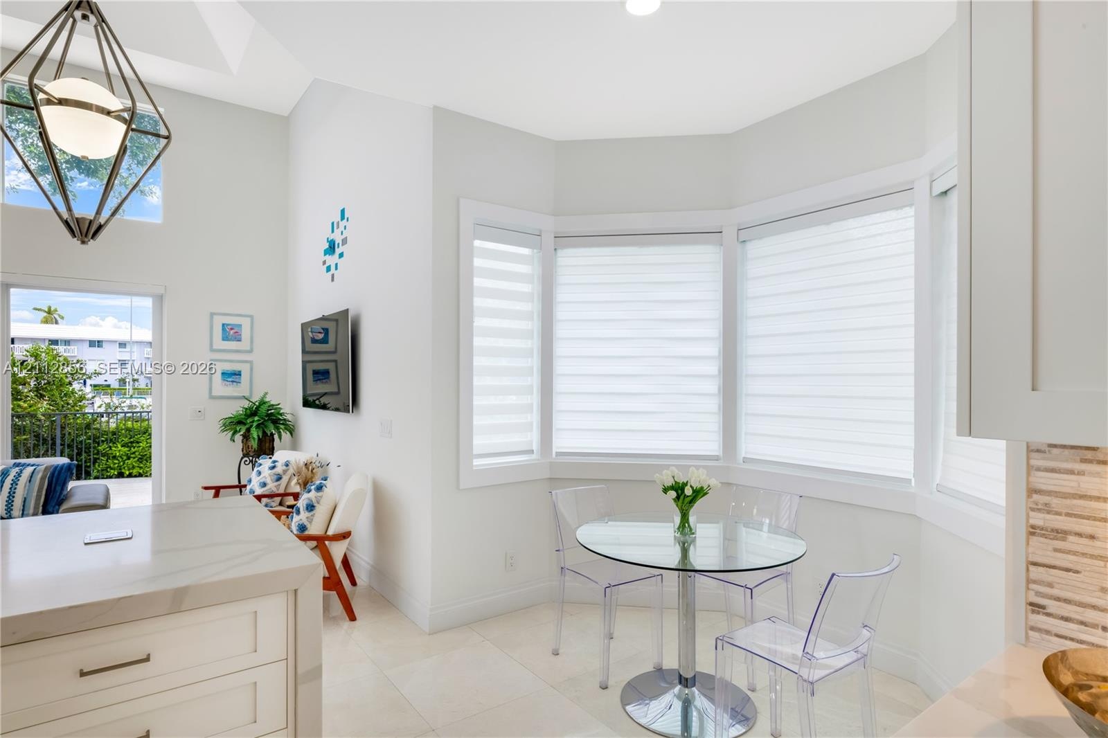 High-ceilinged room featuring a bay window, light-toned tile flooring, a geometric pendant light fixture, and a kitchen island with a stone-finish cou