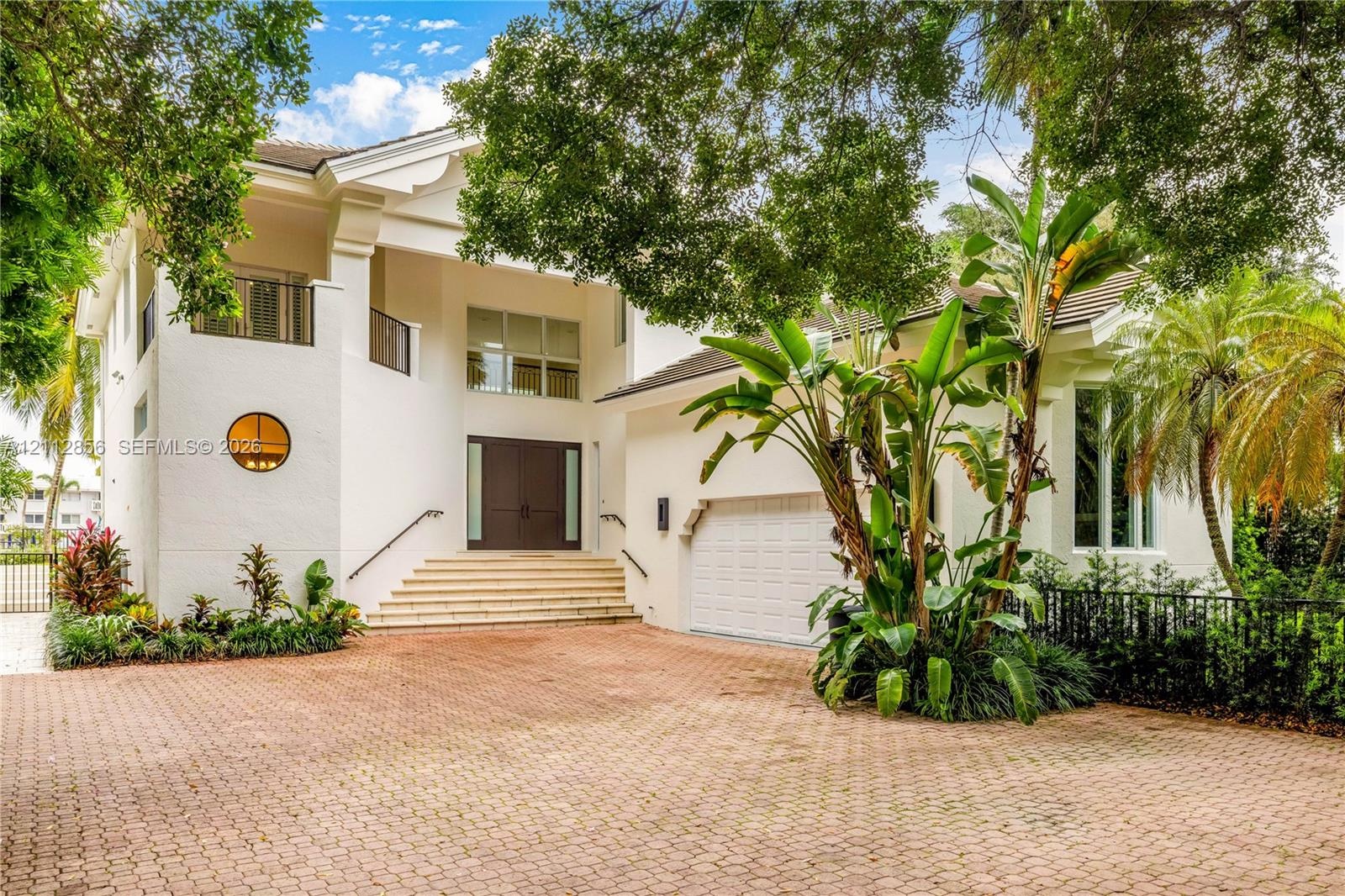 Two-story exterior featuring a paver driveway, double front doors, an elevated entryway with stone steps, a circular accent window, and a built-in gar