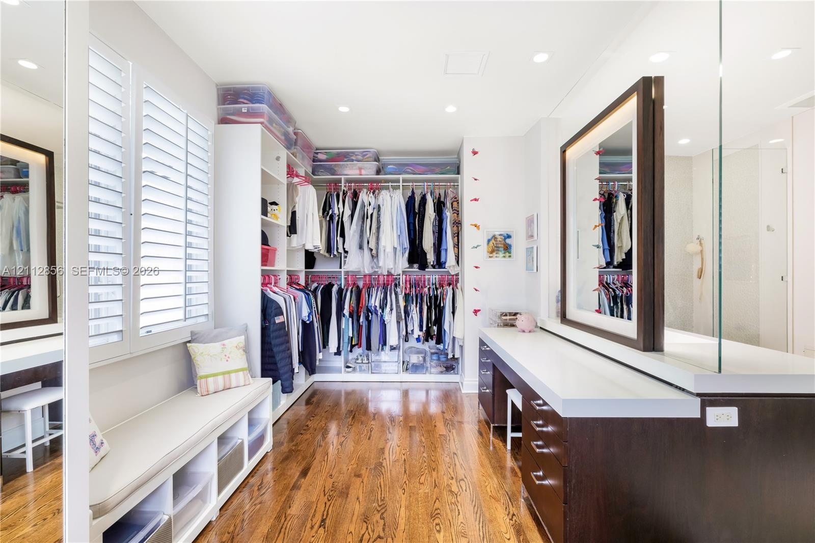 Custom dressing room featuring integrated floor-to-ceiling cabinetry, recessed lighting, wood-finish flooring, plantation shutters, and a built-in van