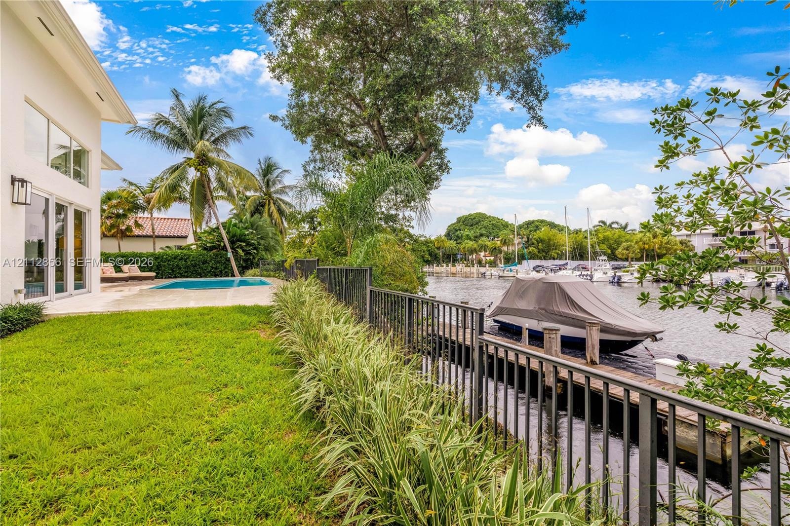 Waterfront property featuring a private boat dock, swimming pool, manicured lawn, and metal perimeter fencing