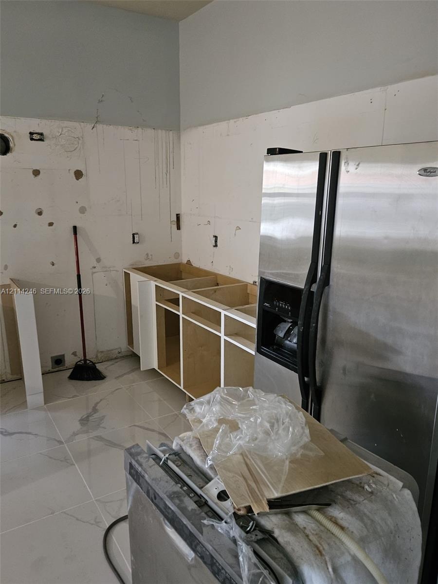 Large-format tile flooring, unfinished cabinetry, and a side-by-side stainless steel refrigerator