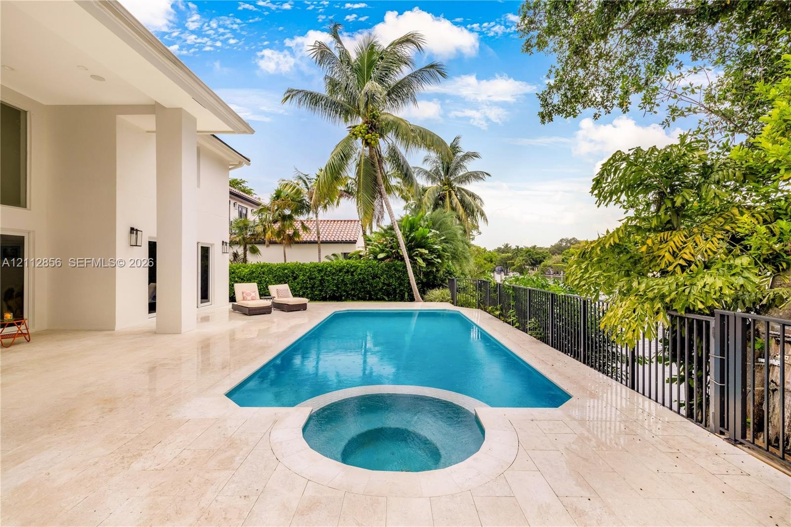 Outdoor living space featuring a tiled pool deck, a swimming pool with an integrated spa, and metal perimeter fencing