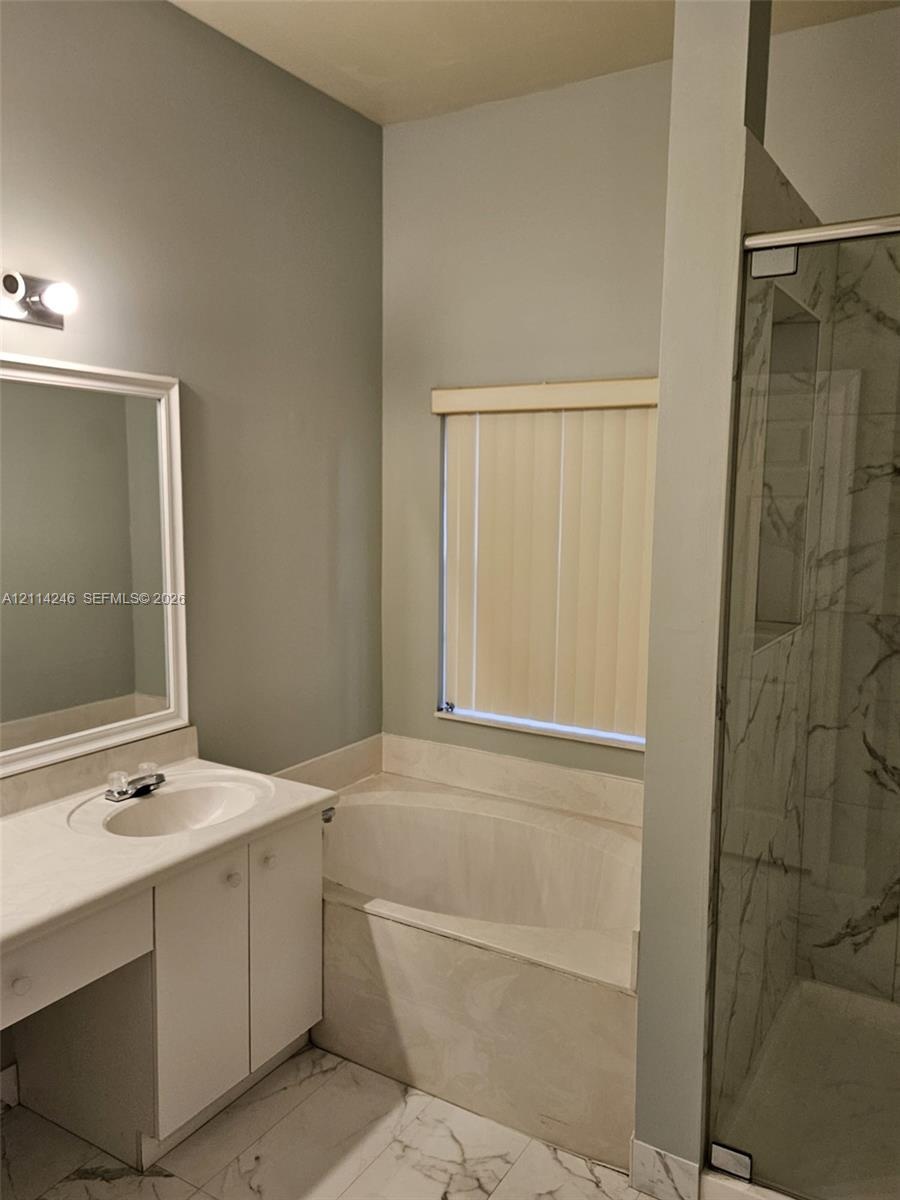 Vanity with integrated sink and countertop, soaking tub with tile surround, glass-enclosed shower with tiled walls, and large-format tile flooring