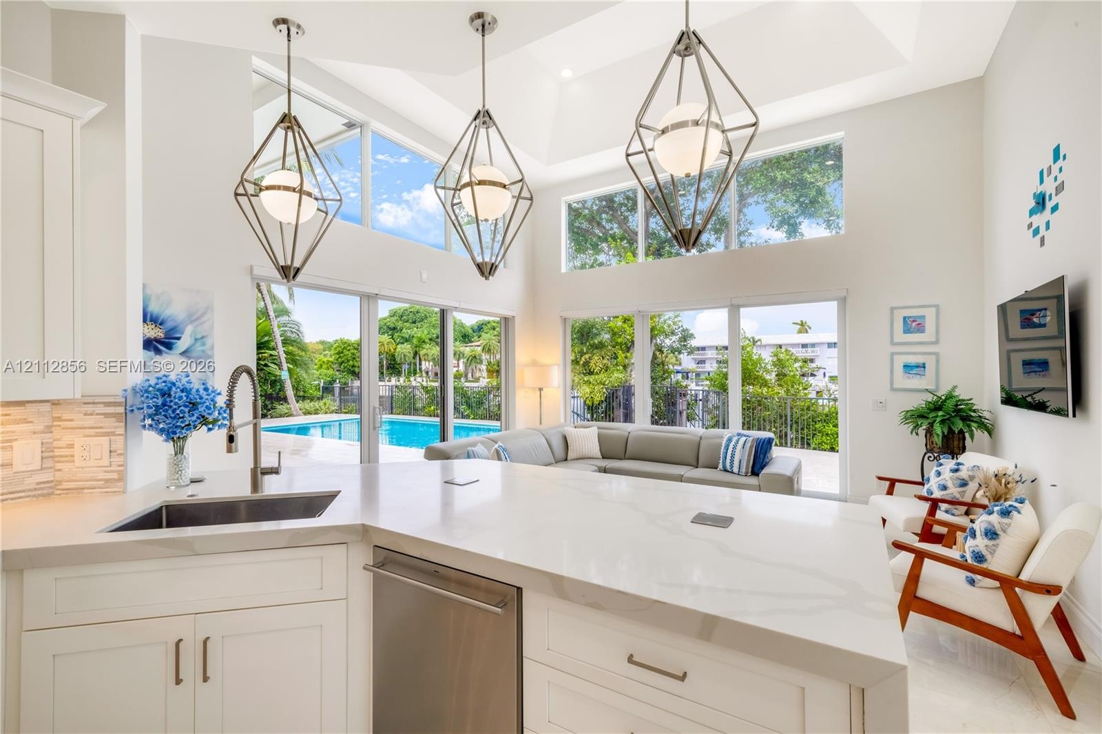 Kitchen island featuring a quartz countertop and stainless steel under-mount sink, high ceilings, geometric metal pendant lighting, and floor-to-ceili