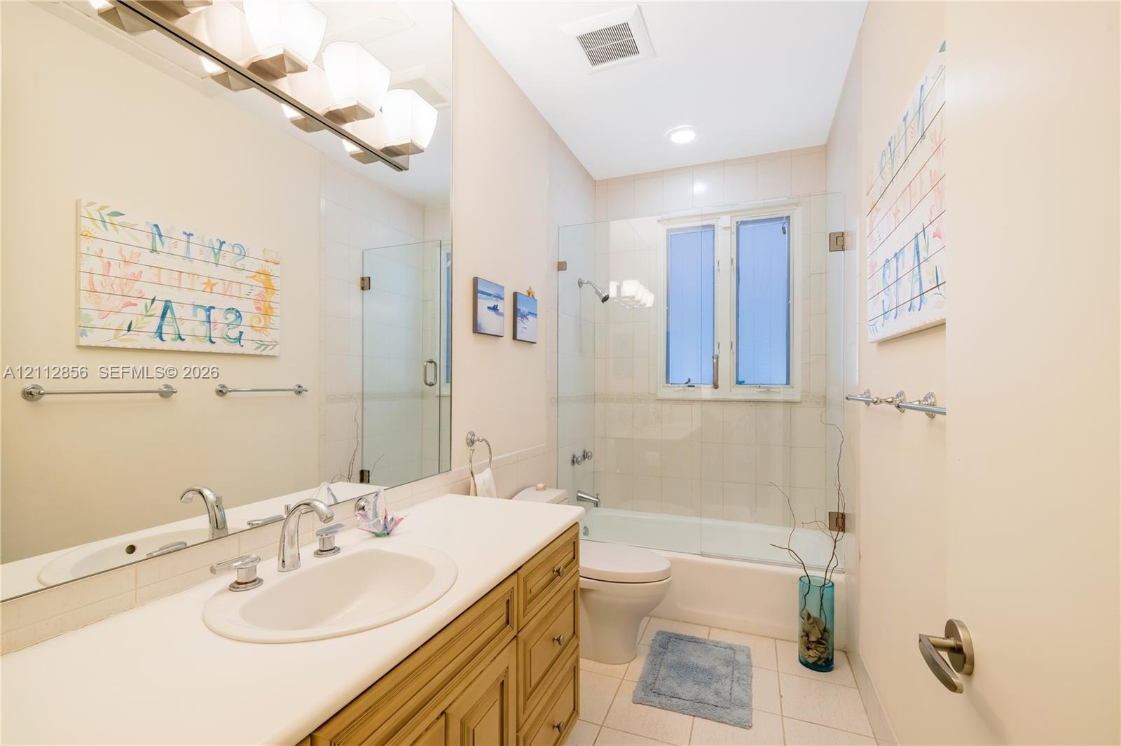 Bathroom featuring wood-finish cabinetry, an integrated sink with a chrome dual-handle faucet, a full-width vanity mirror, and a tub-shower combinatio