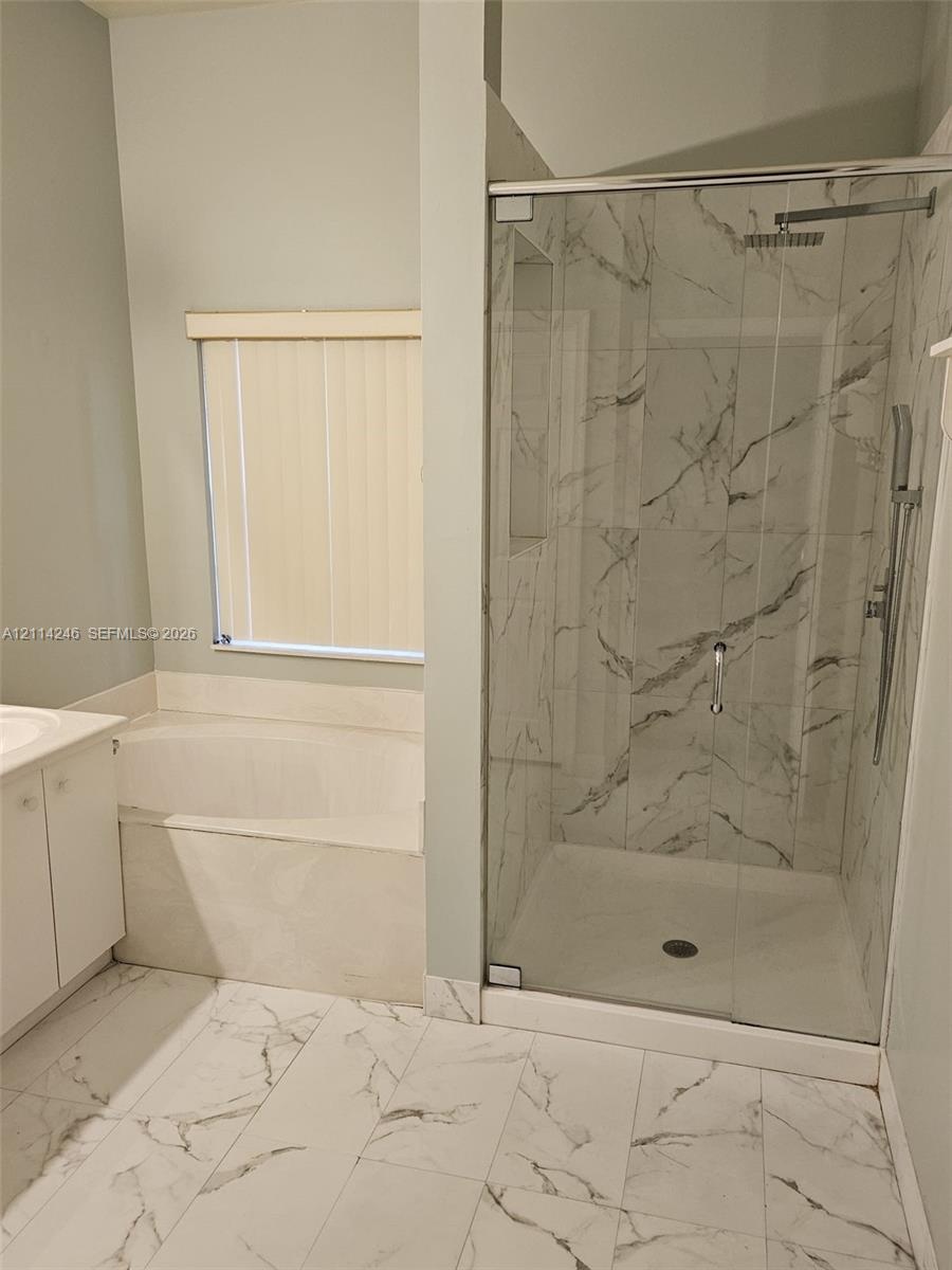 Walk-in shower with stone-finish tile surround, ceiling-mounted rainfall shower head, glass enclosure, built-in soaking tub, and large-format tile flo