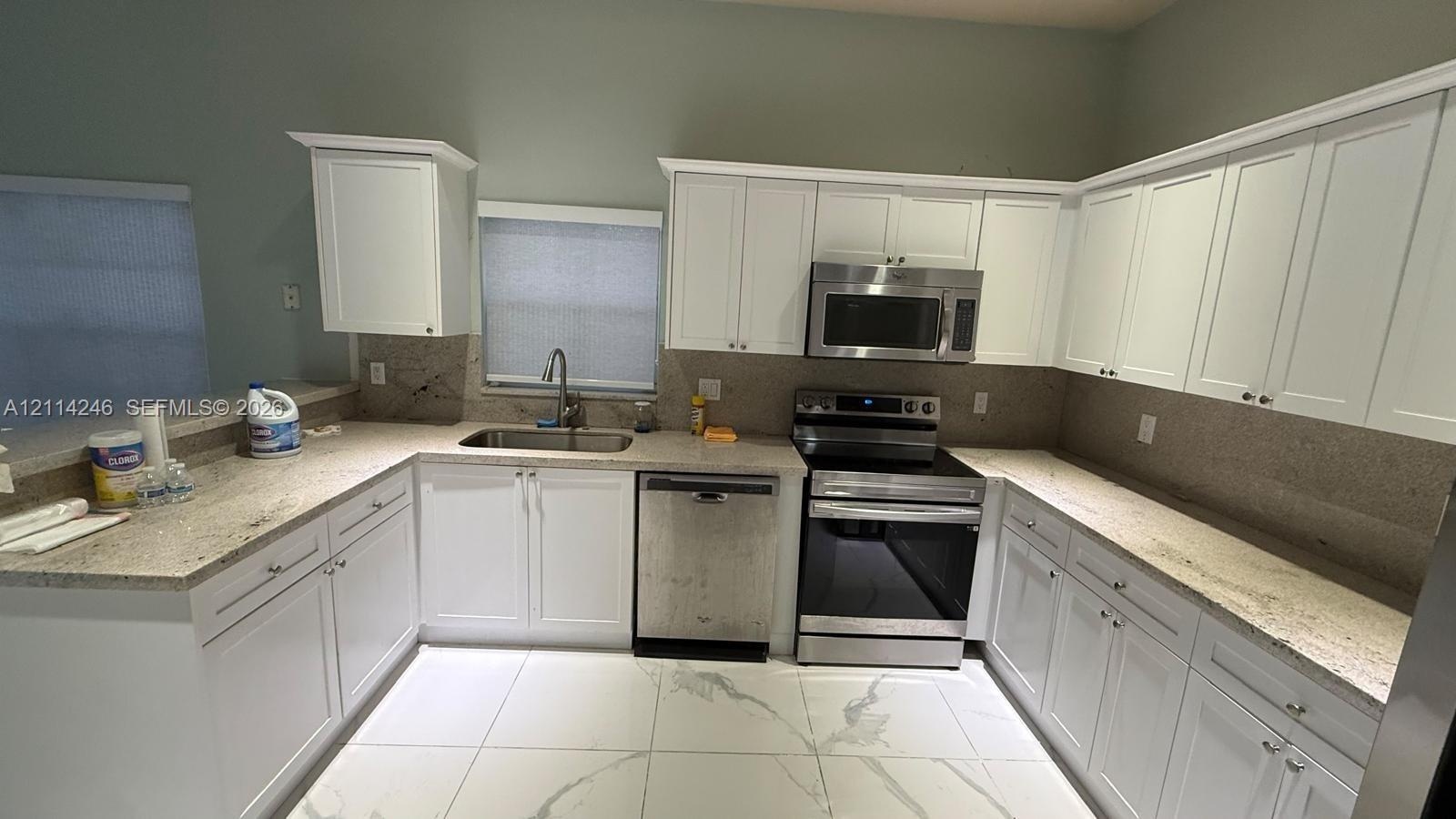 Kitchen featuring white shaker-style cabinetry, stone-finish countertops, stainless steel appliances, an undermount sink, and large-format tile floori