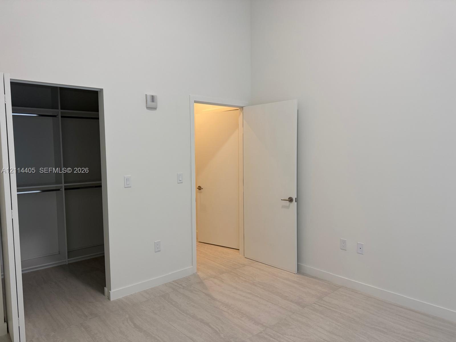 High-ceilinged room featuring light-toned wood-finish flooring, white walls, built-in closet shelving, and solid-core doors with brushed-metal hardwar