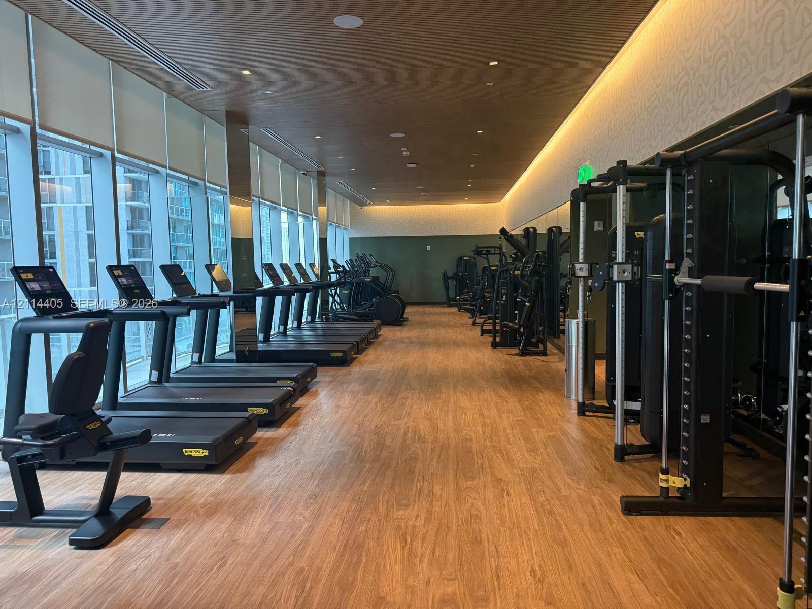 Fitness center featuring wood-finish flooring, floor-to-ceiling windows, recessed cove lighting, and wood-paneled ceiling detail
