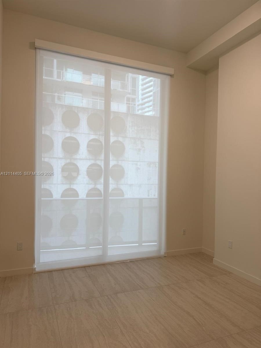 Floor-to-ceiling glass sliding door with white roller shade, neutral tile flooring, and smooth-finish walls