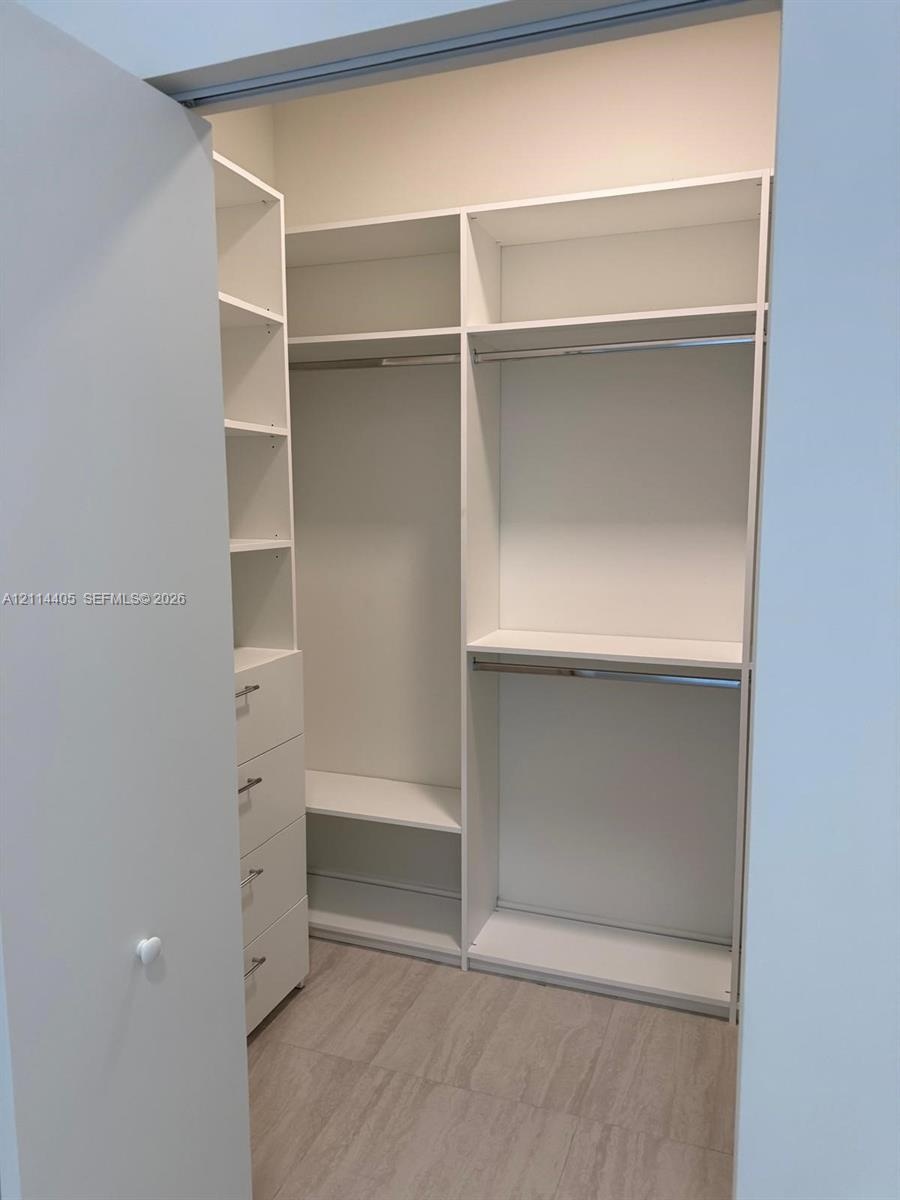 Custom storage system featuring white built-in cabinetry, multiple adjustable shelves, integrated hanging rods, and a four-drawer stack with metallic 