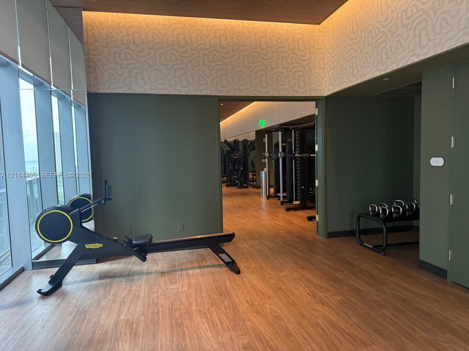 Fitness center featuring floor-to-ceiling windows, wood-finish flooring, recessed cove lighting, and textured wall accents
