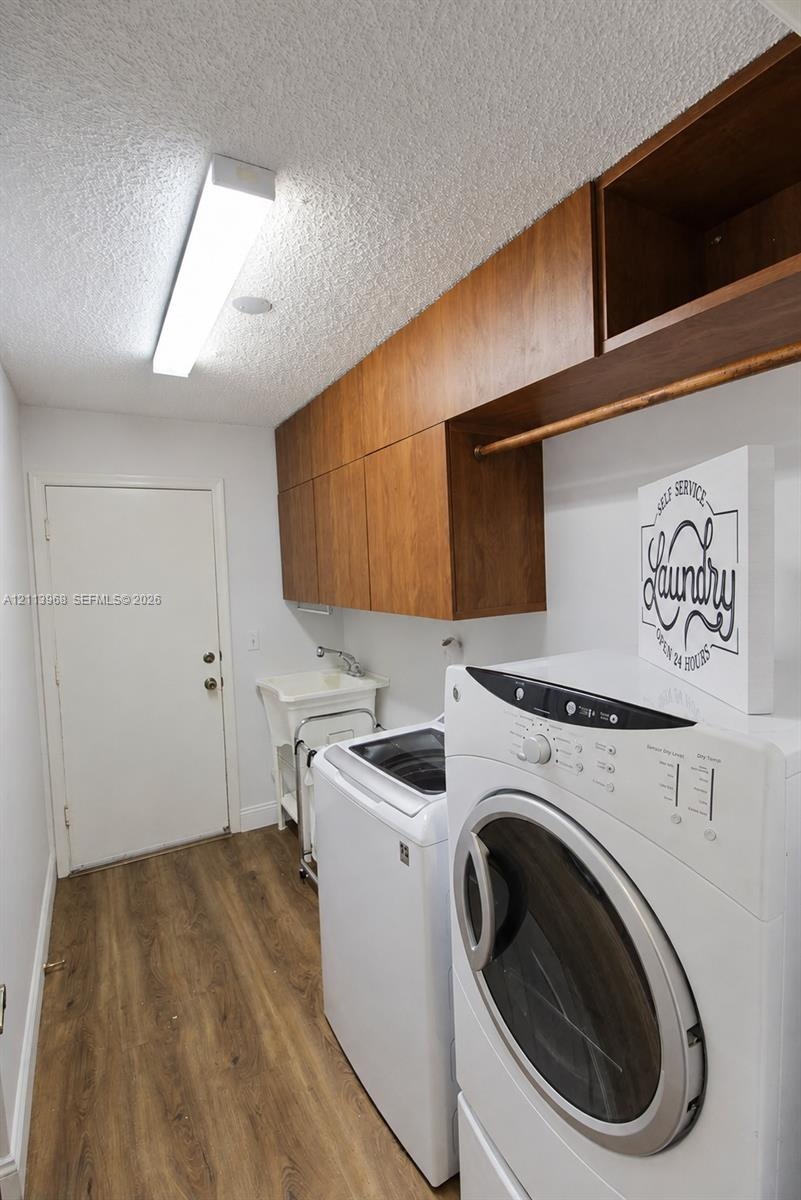 Laundry area featuring wood-finish cabinetry with an integrated hanging rod, wood-finish flooring, a utility sink, and a linear overhead light fixture