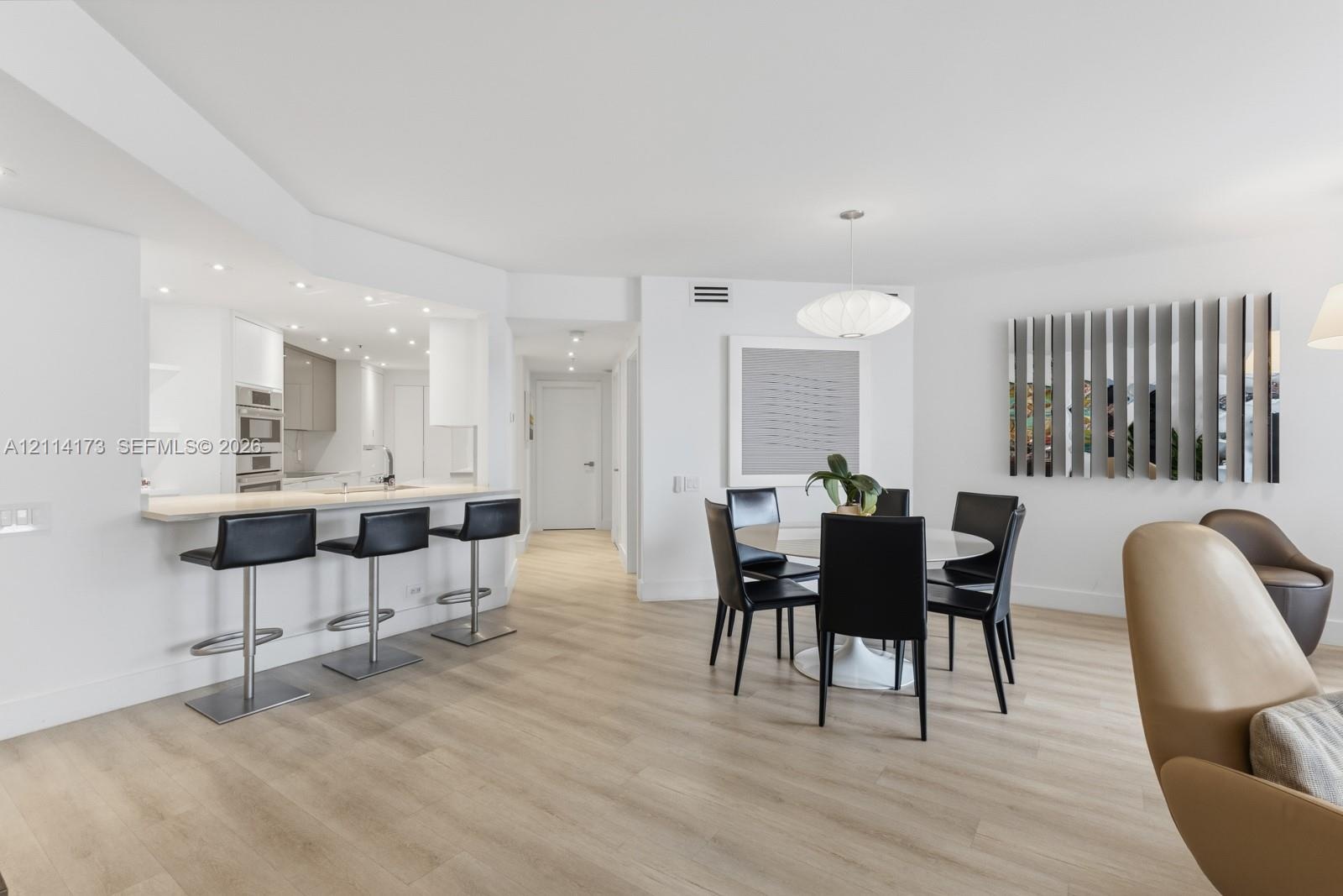 Open-concept space featuring light wood-finish flooring, recessed lighting, built-in kitchen cabinetry with integrated stainless steel appliances, and