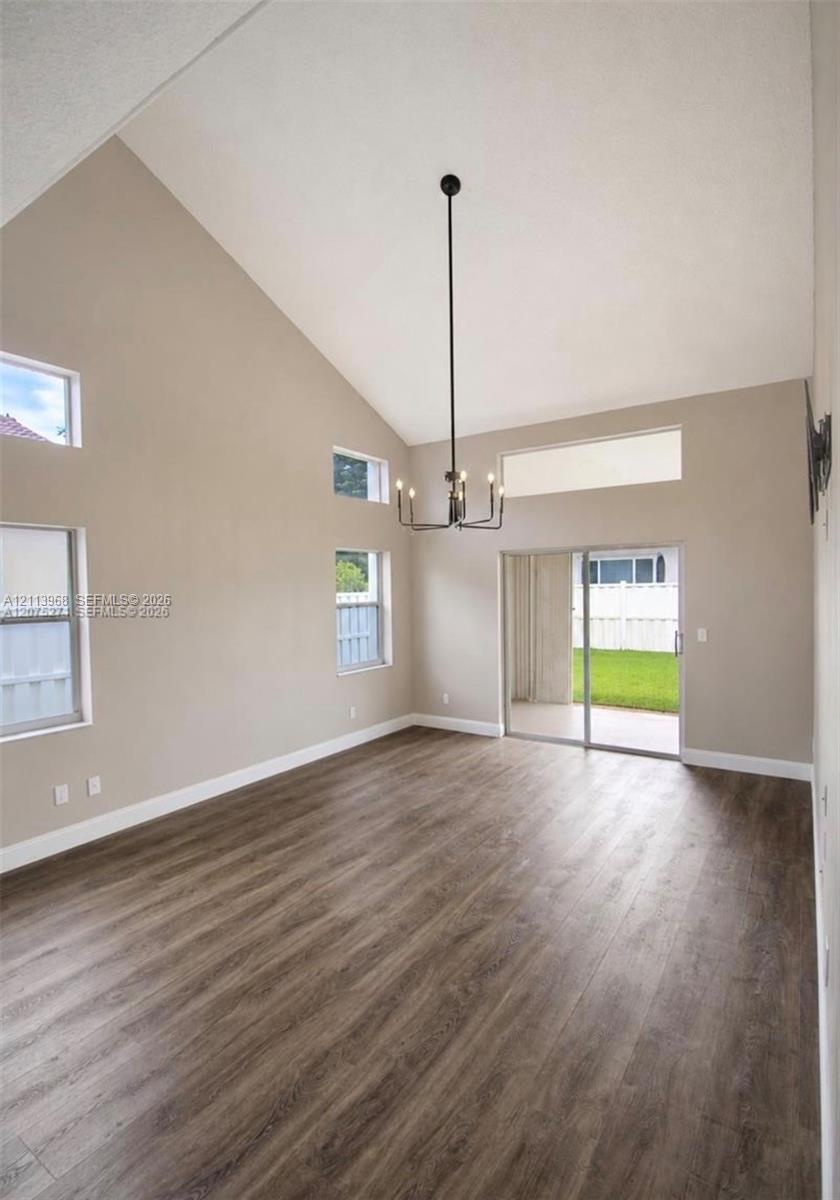 Vaulted ceilings, wood-finish flooring, multi-level windows, modern chandelier, and sliding glass doors