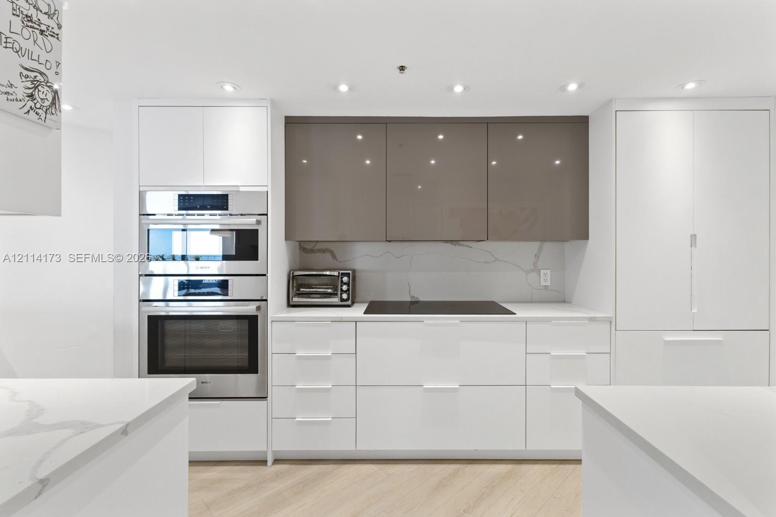 Modern kitchen featuring flat-panel high-gloss cabinetry, stone countertops with veining detail, integrated cooktop, built-in stainless steel double o