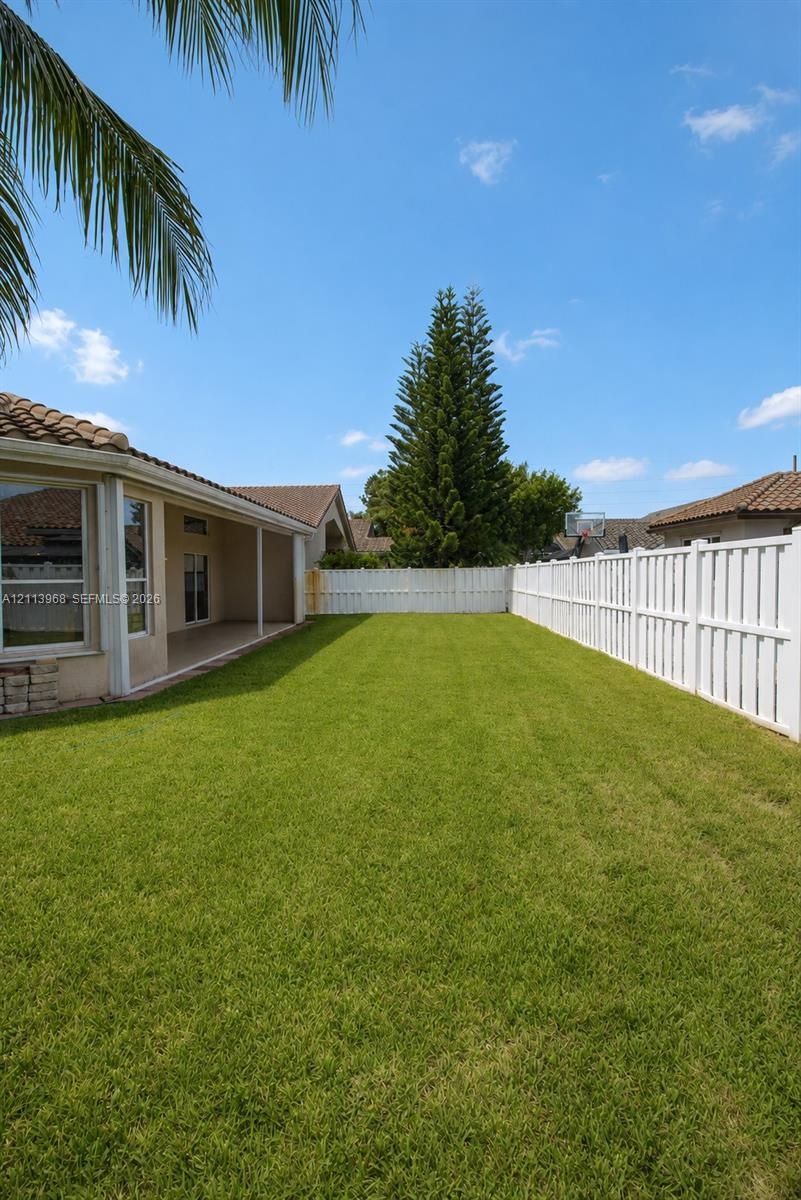 Expansive backyard featuring a level lawn, covered patio, and perimeter white vinyl privacy fencing