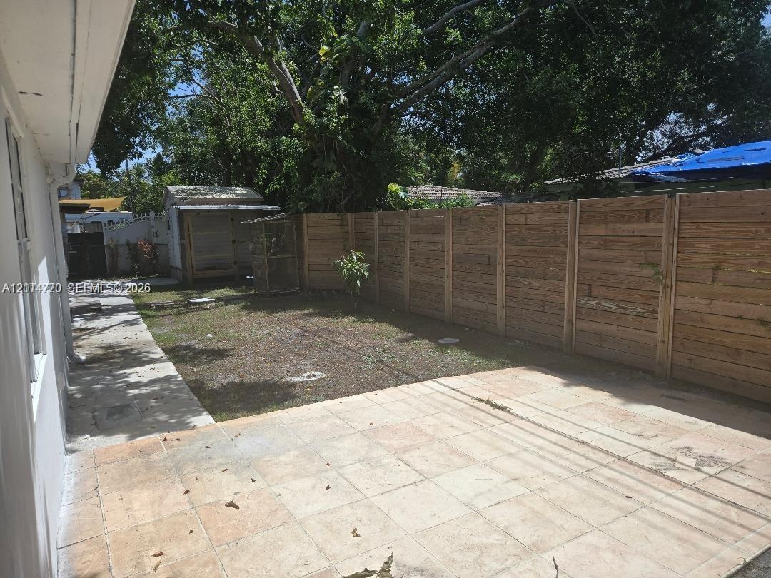 Rear outdoor space featuring a paved tile patio, a horizontal wood-slat privacy fence, and an integrated exterior storage structure