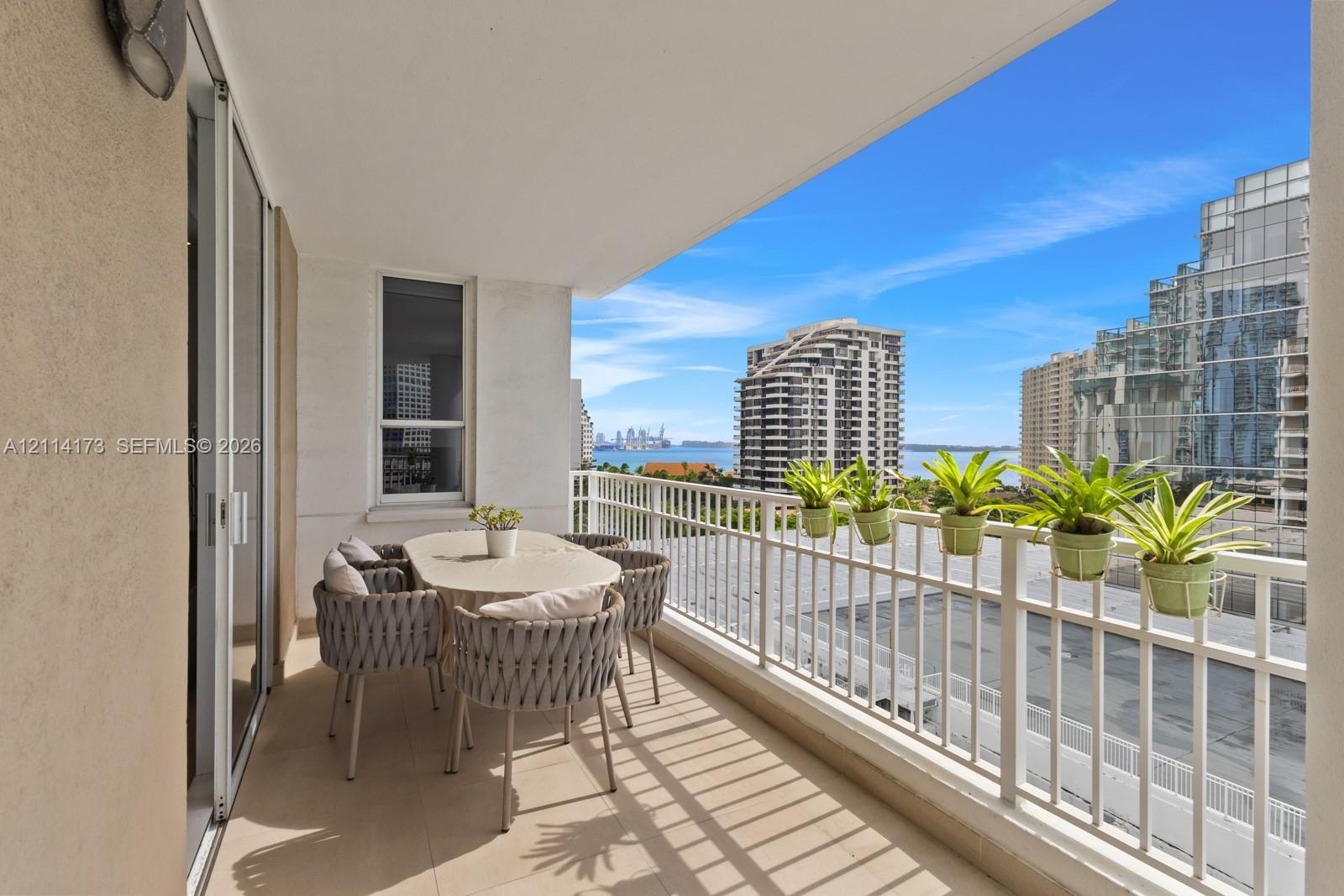 Covered balcony with neutral tile flooring, white metal railing, and sliding glass door access