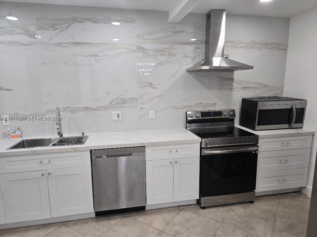 Kitchen featuring white cabinetry, large-format stone-patterned tile backsplash, stainless steel appliances, and solid surface countertops