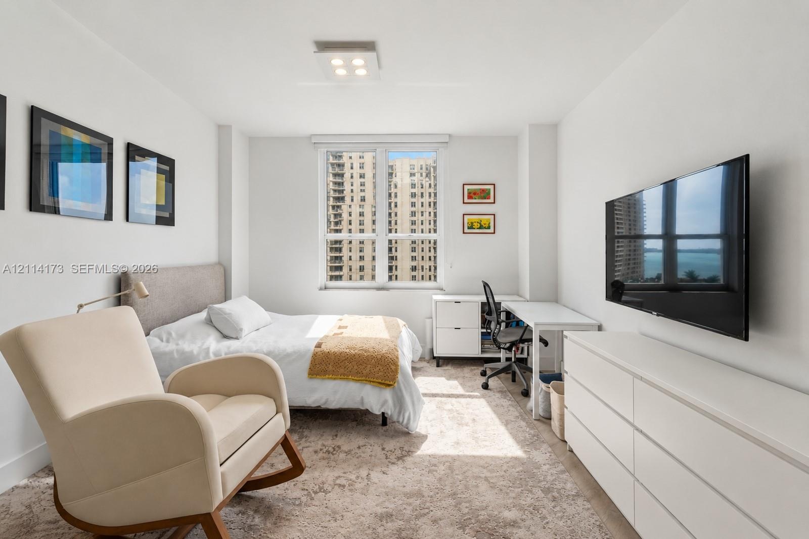 Bright interior space featuring a large window with urban and water scenery, neutral wall finishes, and a modern ceiling-mounted light fixture