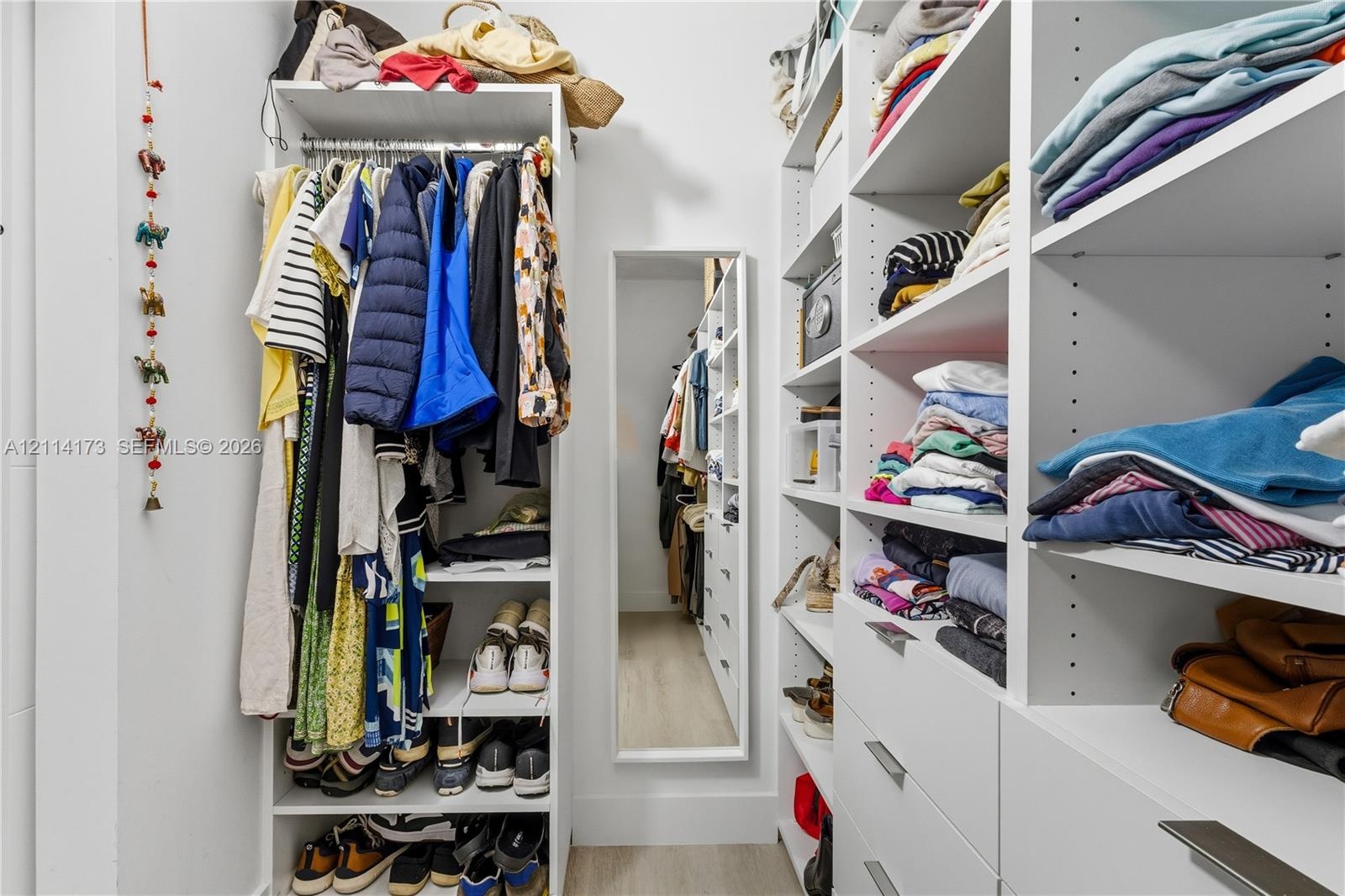 Walk-in closet featuring extensive built-in white shelving, integrated clothing rods, multiple pull-out drawers with metal hardware, and a full-length