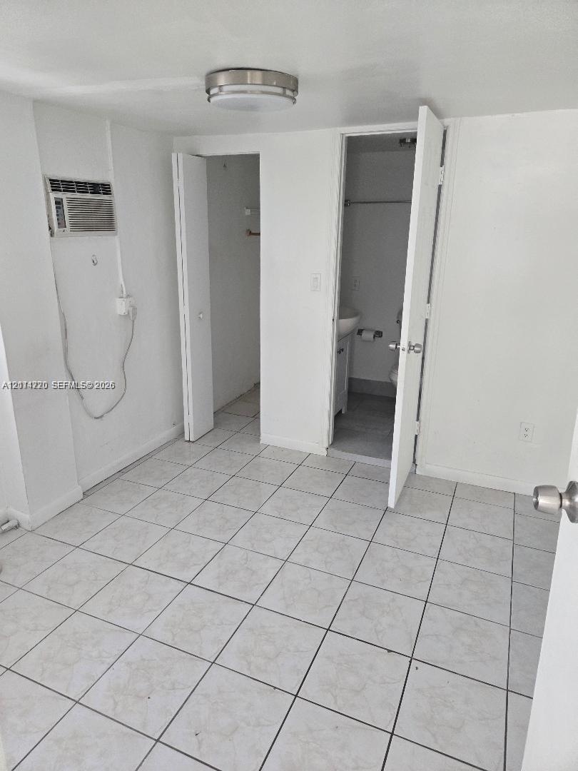 Room featuring neutral tile flooring, a wall-mounted cooling unit, ceiling-mounted lighting, and double-door closet storage