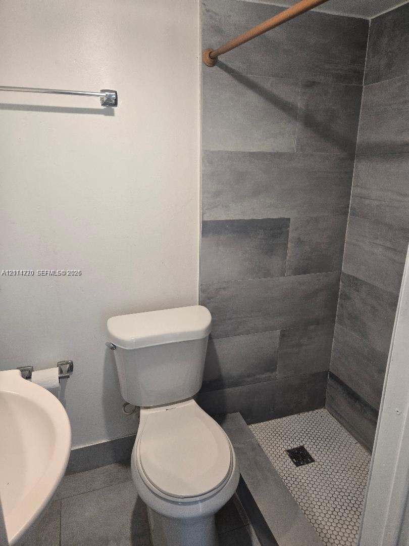 Bathroom featuring a shower stall with large-format stone-finish wall tile, a mosaic-tiled floor, a pedestal sink, and a high-profile toilet