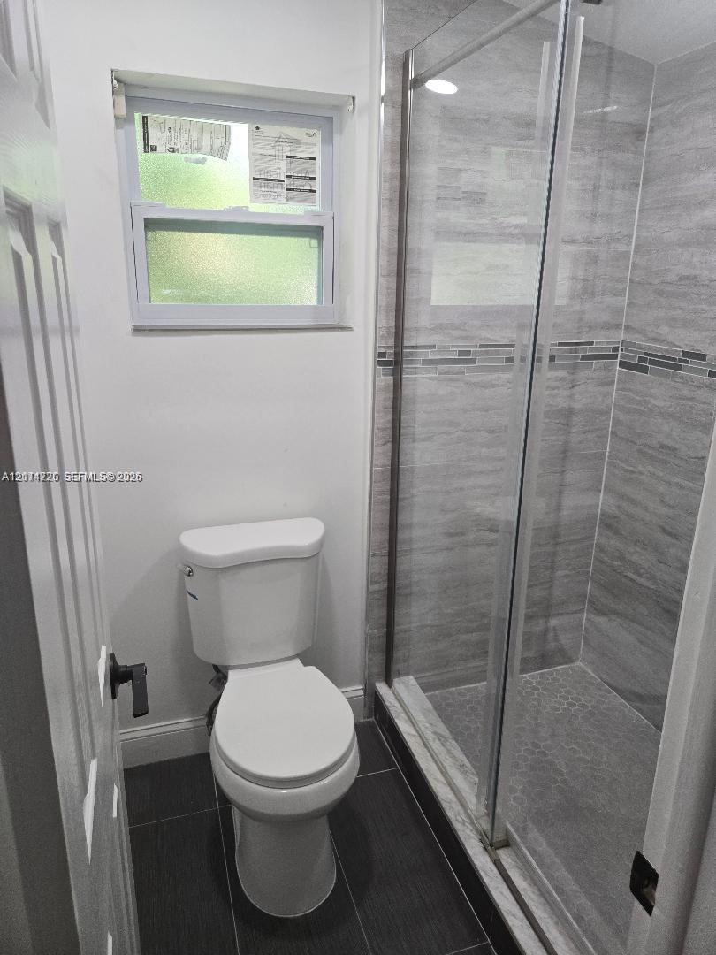 Glass-enclosed shower with horizontal wall tile, mosaic accent strip, and dark floor tiling, complemented by a single-flush toilet and a horizontal sl
