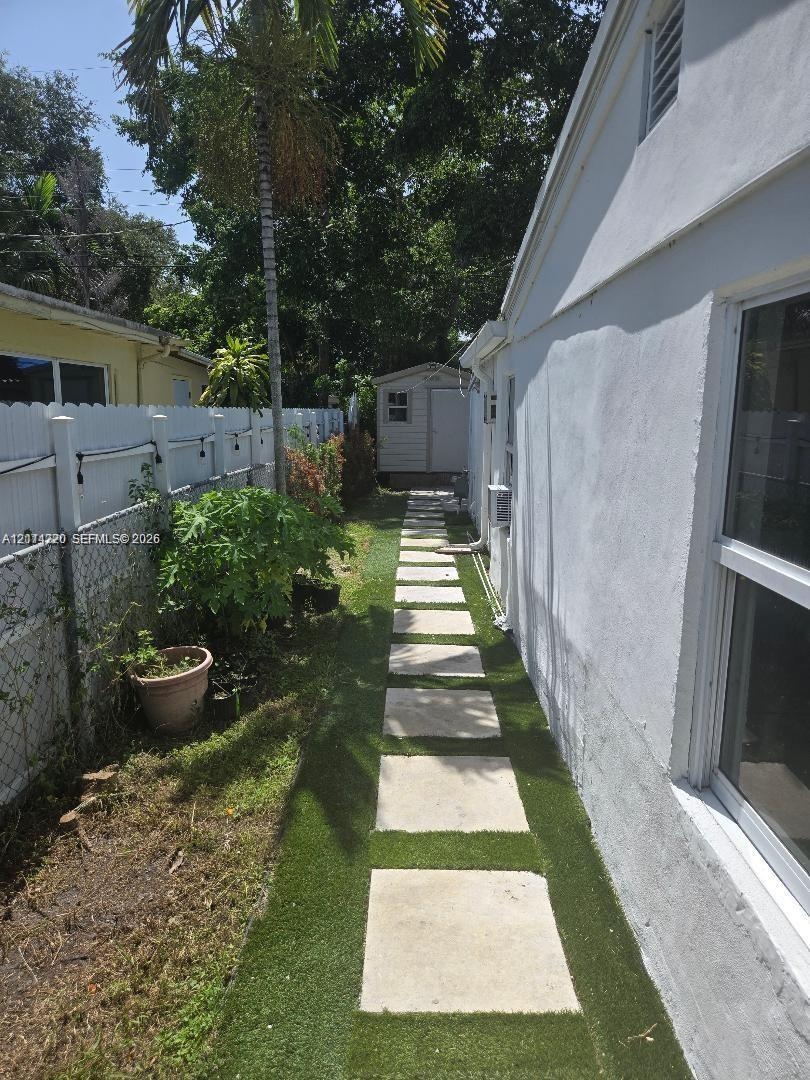 Side yard featuring a concrete paver walkway, artificial turf landscaping, white vinyl privacy fencing, and a detached storage structure