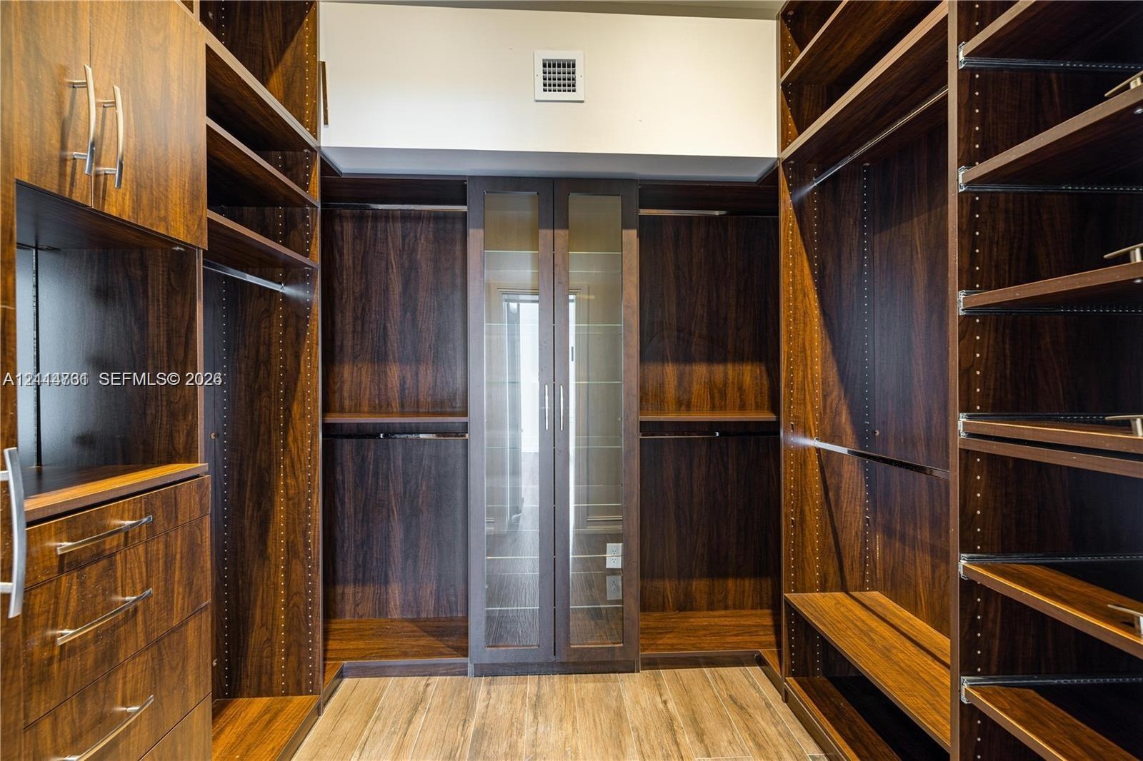 Custom walk-in closet featuring wood-finish cabinetry, built-in drawer units, adjustable shelving, integrated hanging rods, and glass-front cabinetry 