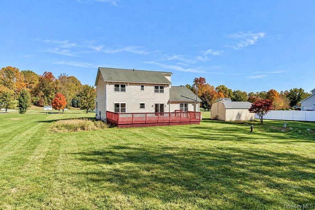 Two-story residence featuring light-toned vinyl siding, a multi-level wood deck, a standalone storage structure, and expansive lawn space
