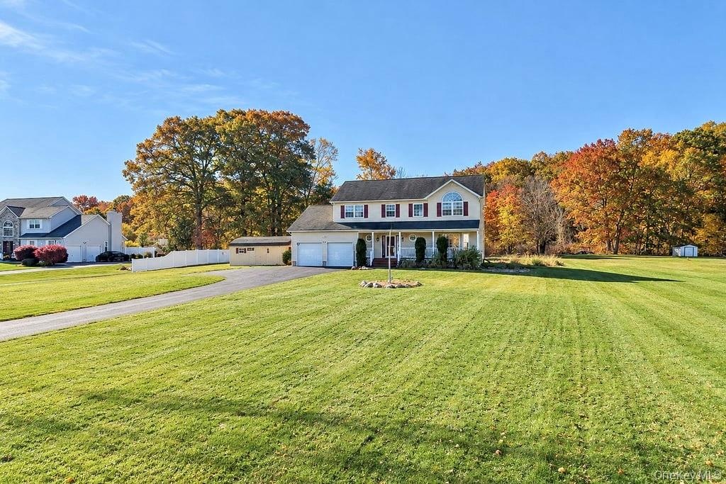 Two-story residence featuring a covered front porch, attached two-car garage, expansive lawn, and a dedicated storage structure