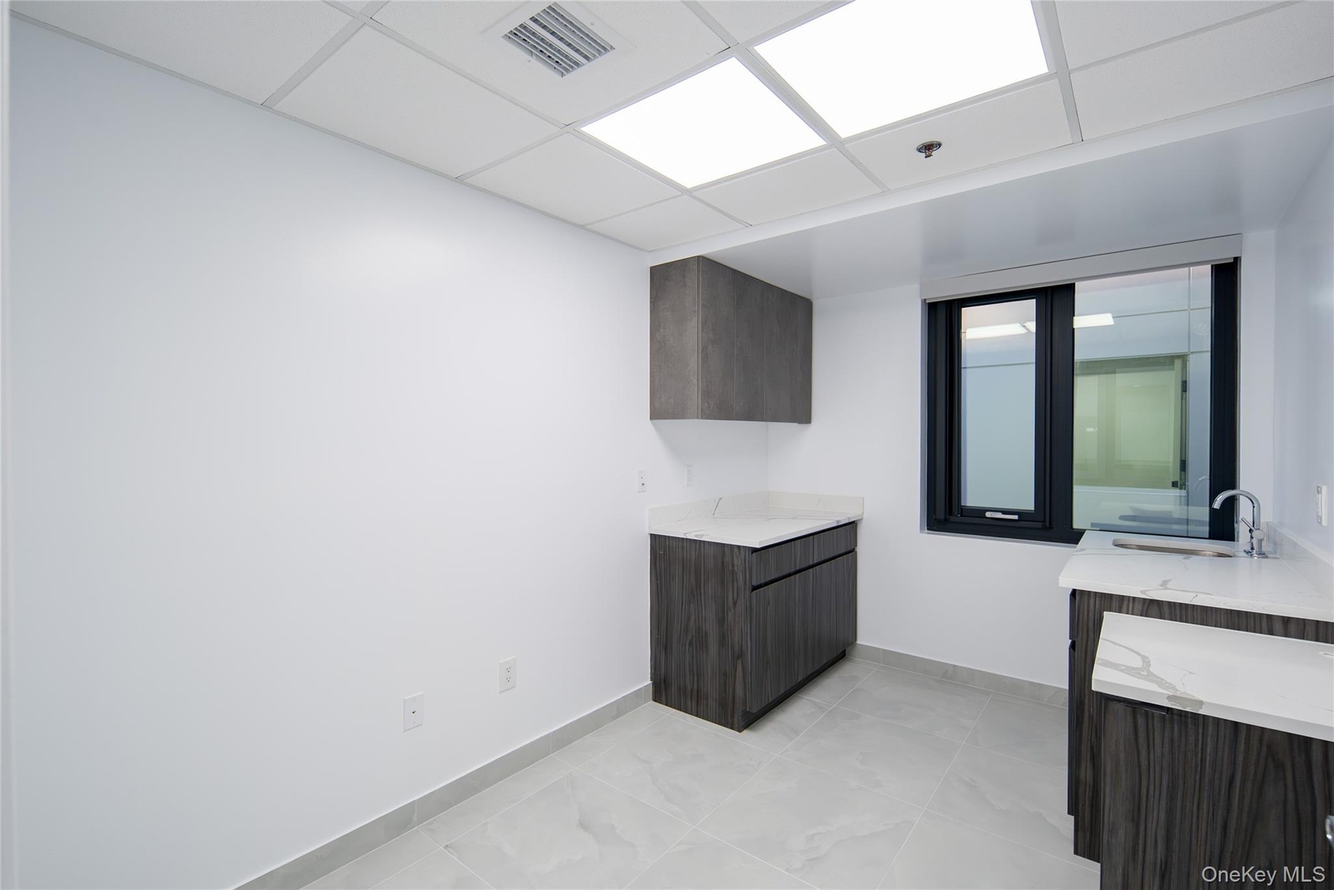 Bar area with dark brown cabinets, a drop ceiling, light stone counters, modern cabinets, and light tile patterned floors