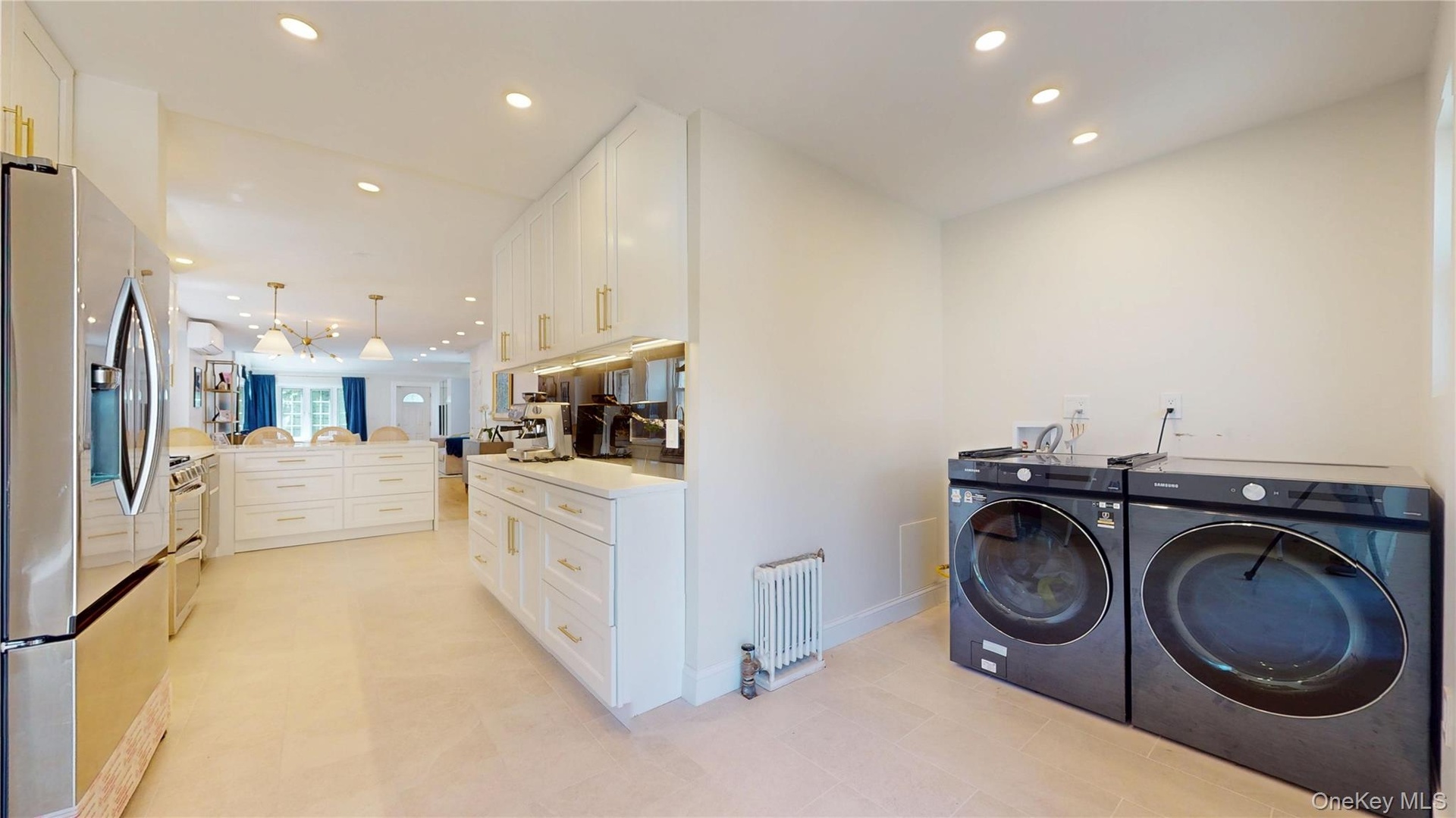 Expansive kitchen and laundry area featuring light-toned flooring, recessed lighting, and white cabinetry with gold-toned hardware