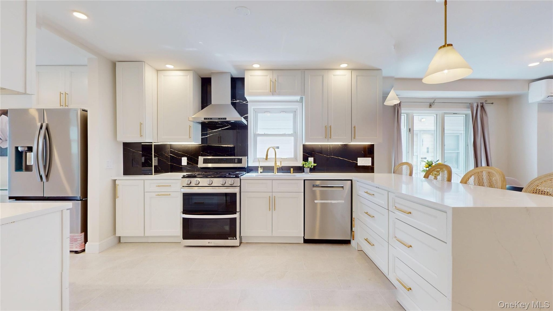 Modern kitchen featuring white cabinetry with gold-tone hardware, stainless steel appliances, and a dark stone backsplash