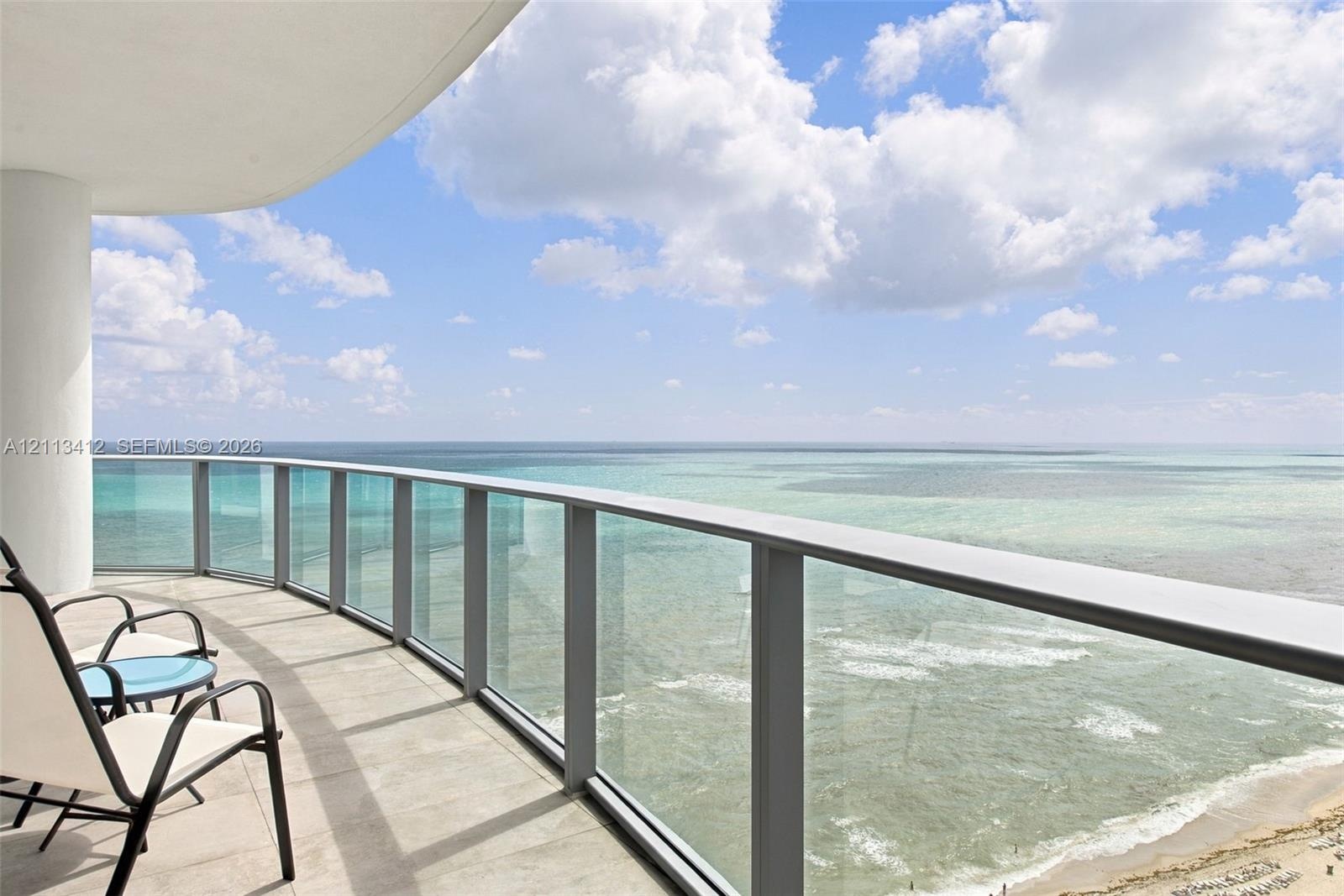 Curved balcony featuring neutral stone-finish flooring and a glass-paneled railing