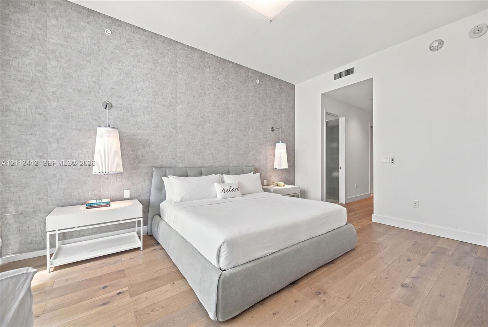 Textured gray accent wall featuring dual wall-mounted pendant lights and wide-plank wood-finish flooring