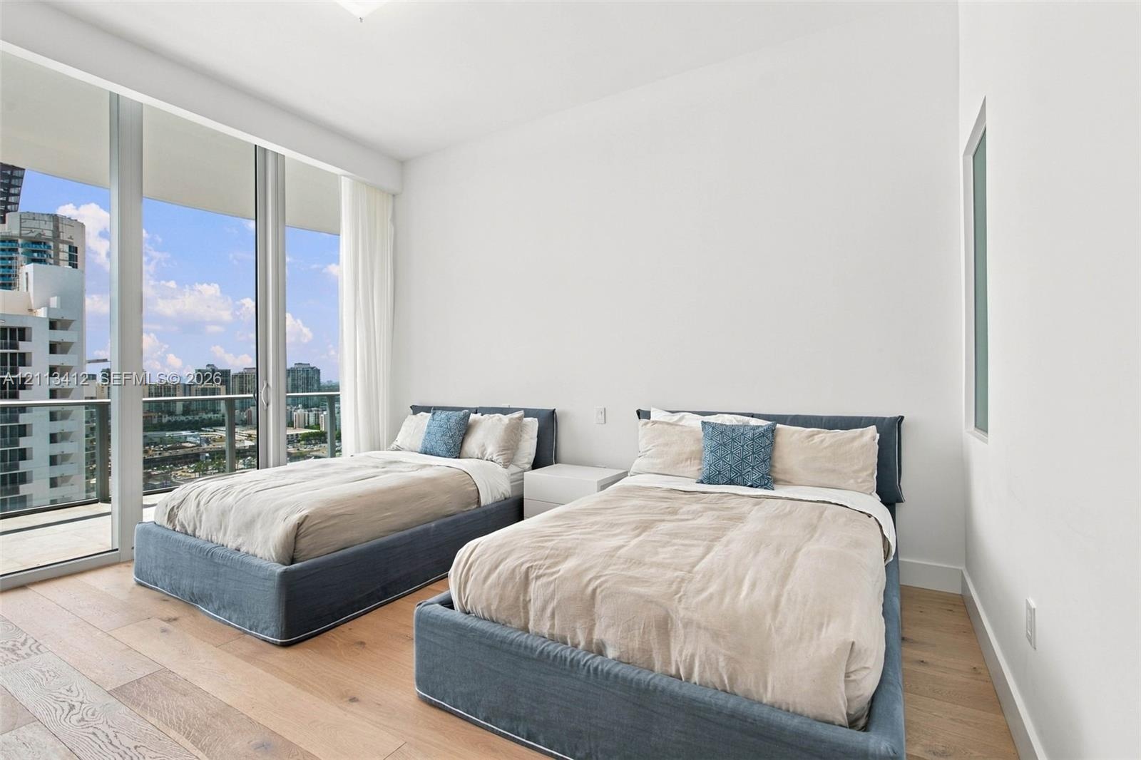 Floor-to-ceiling glass windows, wide-plank wood-finish flooring, and a private balcony with glass railing