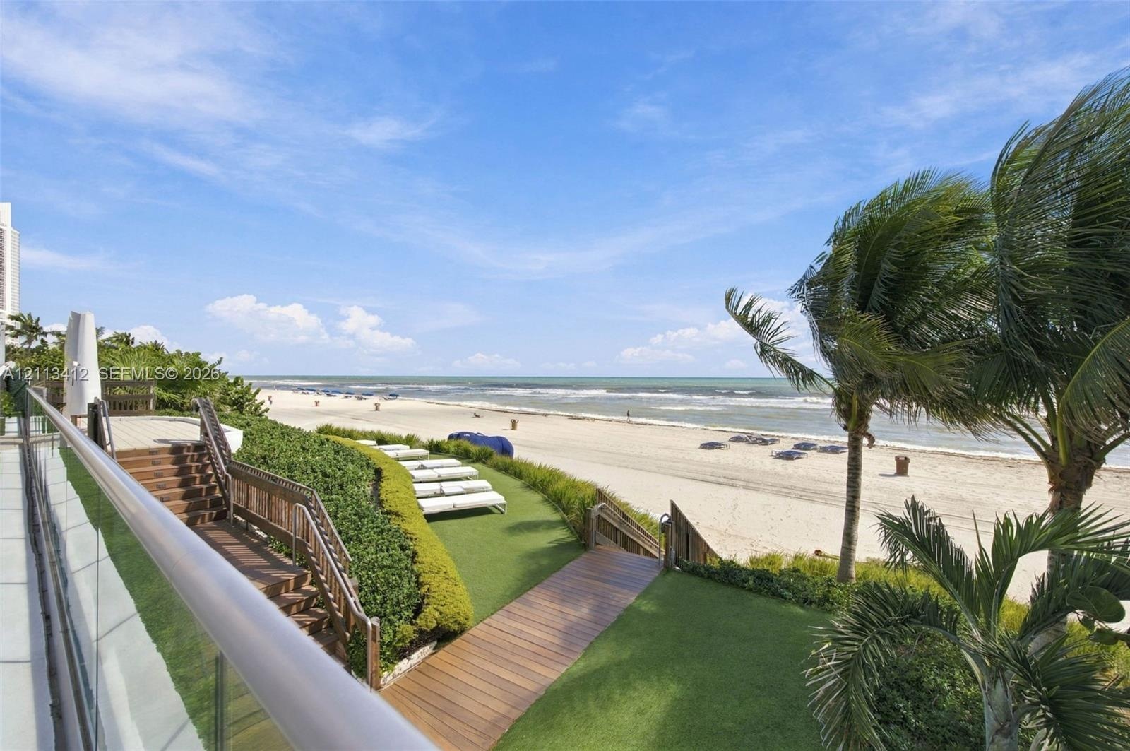 Outdoor terrace featuring glass paneled railings, wood-finish decking, tiered stairways, and private beach access