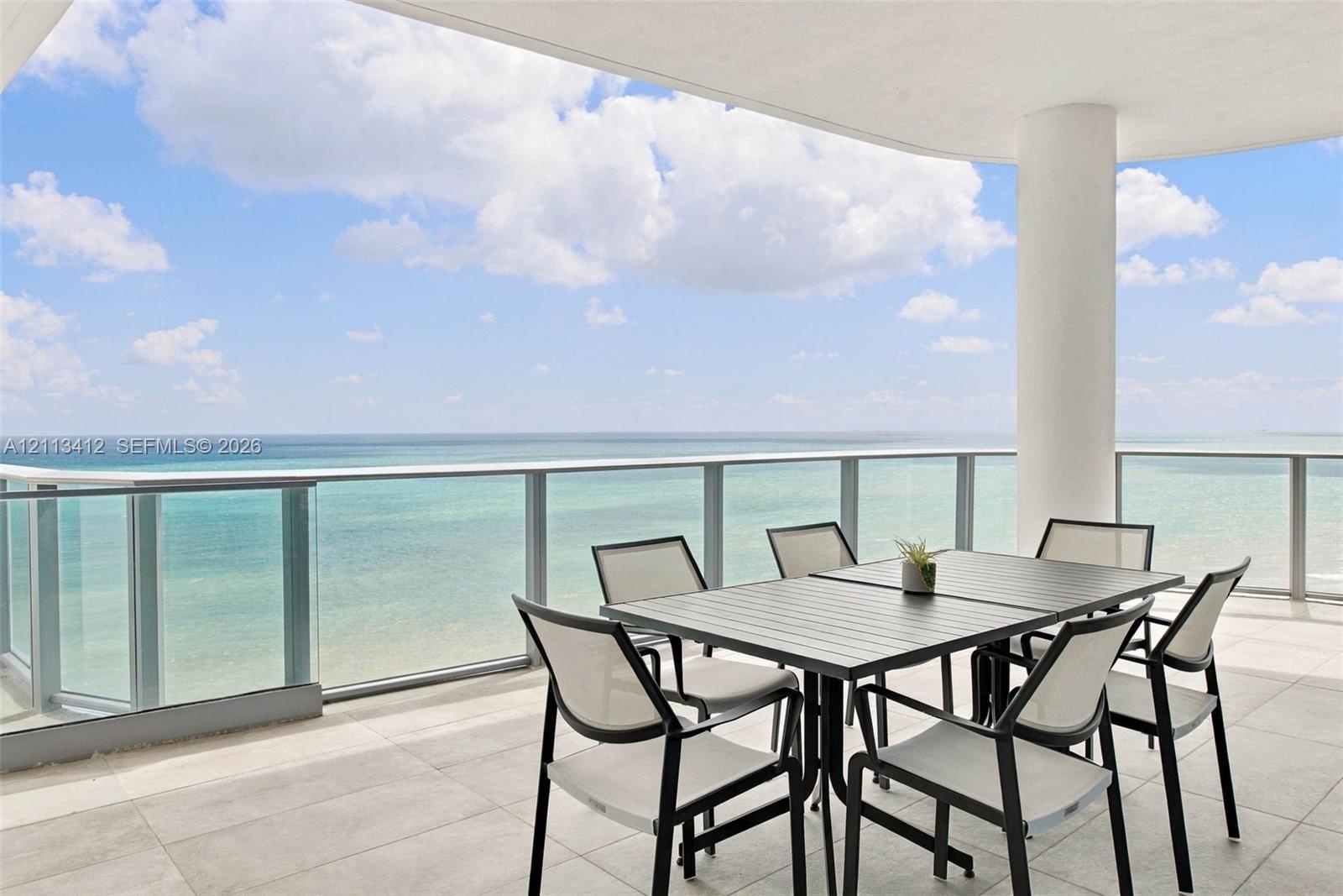 Covered balcony featuring oversized stone-style tile flooring, glass panel railings, and a structural support column