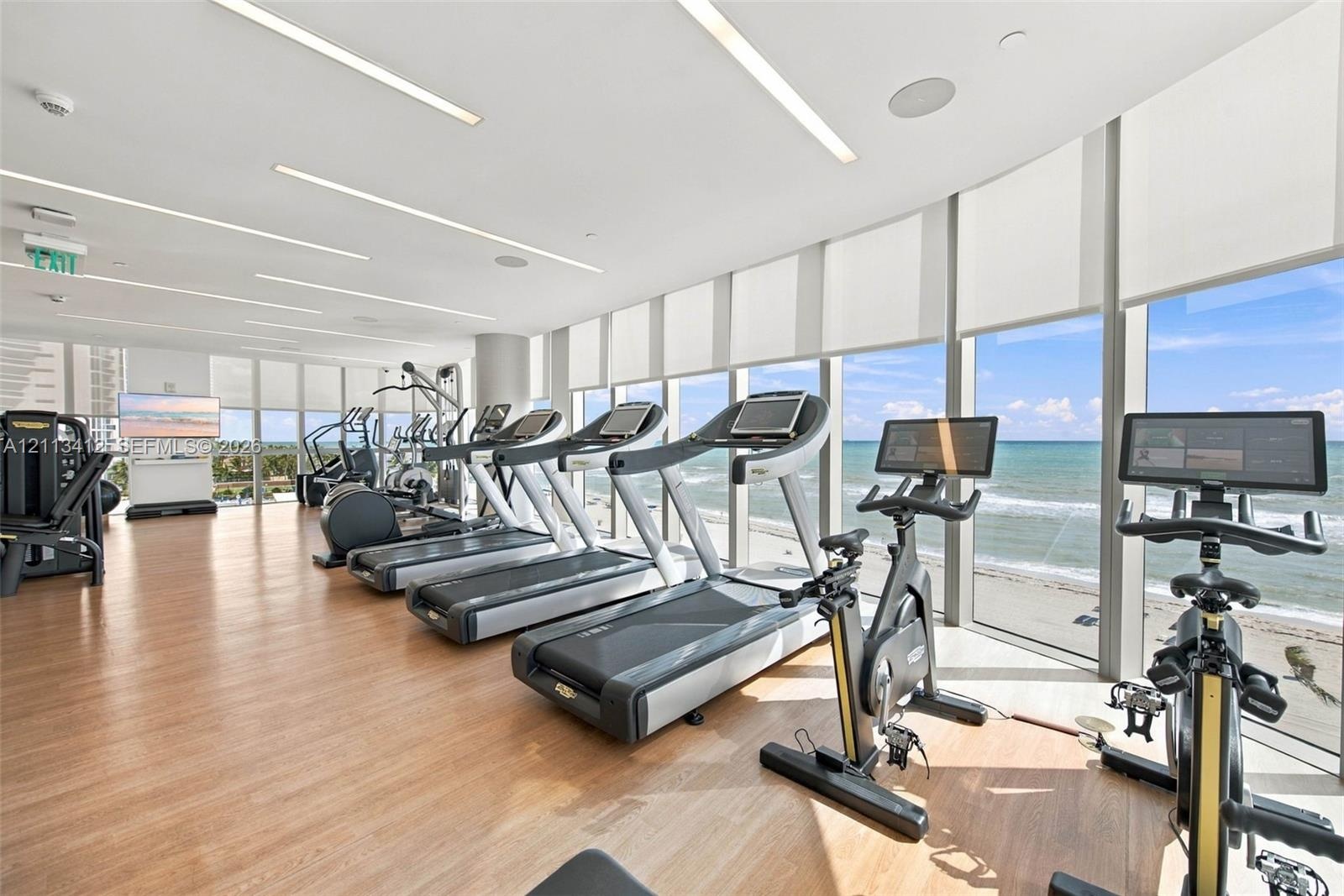 Fitness center featuring wood-finish flooring, floor-to-ceiling windows, and recessed linear lighting, with direct ocean backdrop