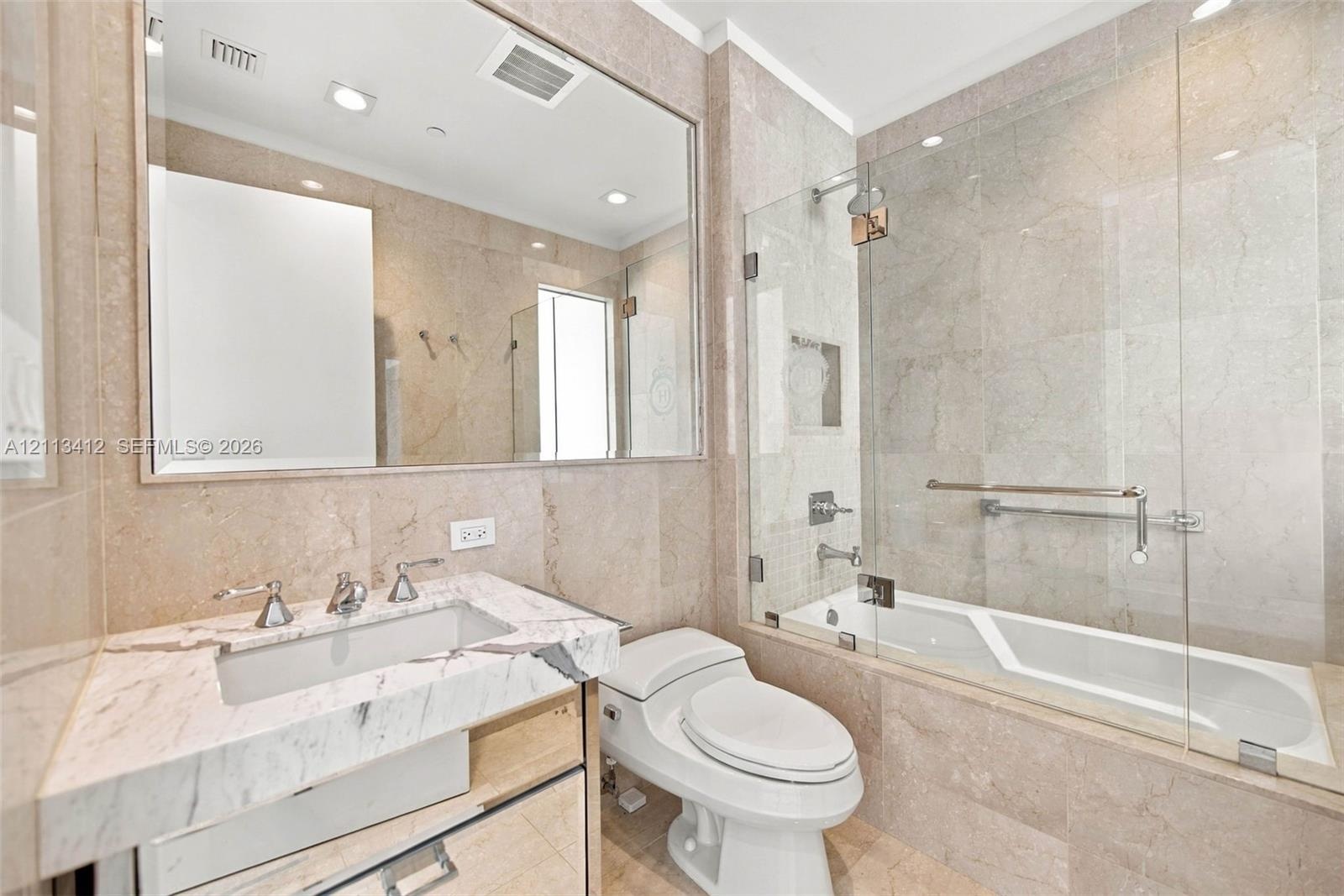 Full-height stone wall tiling, custom vanity with a stone countertop and undermount sink, frameless glass shower enclosure, and a large wall-mounted m