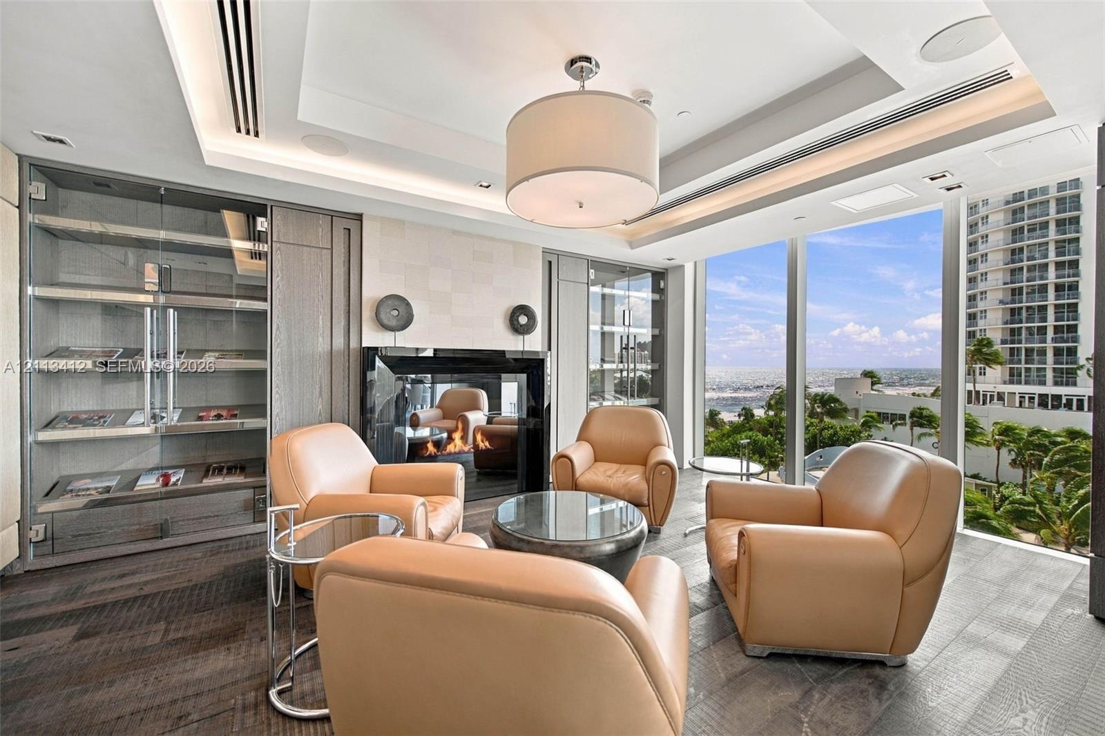 Floor-to-ceiling windows, wood-finish flooring, built-in display cabinetry, tray ceiling with recessed lighting, and a modern fireplace with a black g