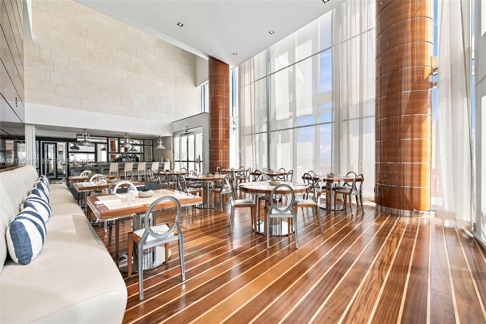 Double-height space featuring floor-to-ceiling glass, inlaid wood-finish flooring, decorative cylindrical columns with wood-toned cladding, and textur
