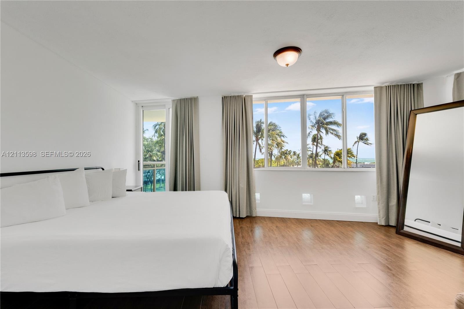 Wood-finish flooring, floor-to-ceiling windows, flush-mount ceiling lighting, and a glass-paneled door leading to an exterior balcony