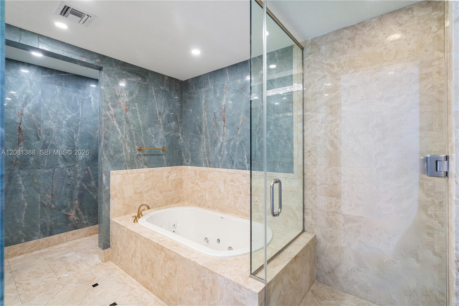 Bathroom featuring full-height blue and beige stone wall tile, recessed lighting, a built-in jetted soaking tub with gold-tone fixtures, and a framele