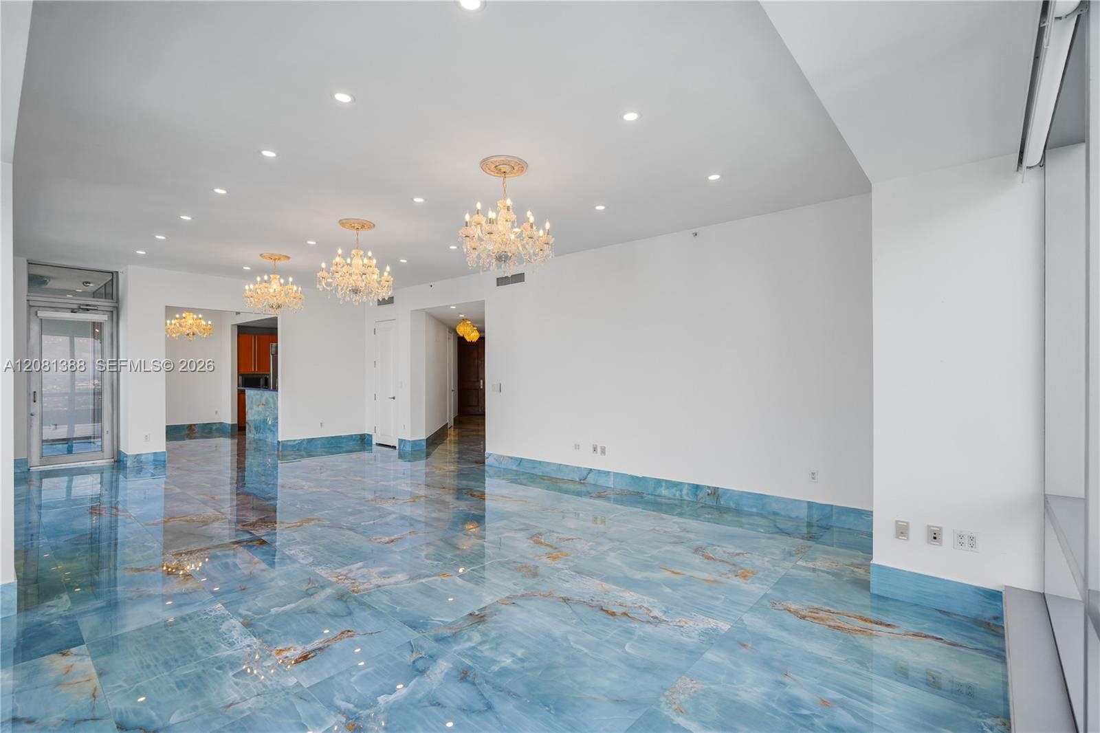 Open interior featuring polished blue stone flooring, recessed ceiling lighting, three ornate crystal chandeliers, and floor-to-ceiling glass panel do
