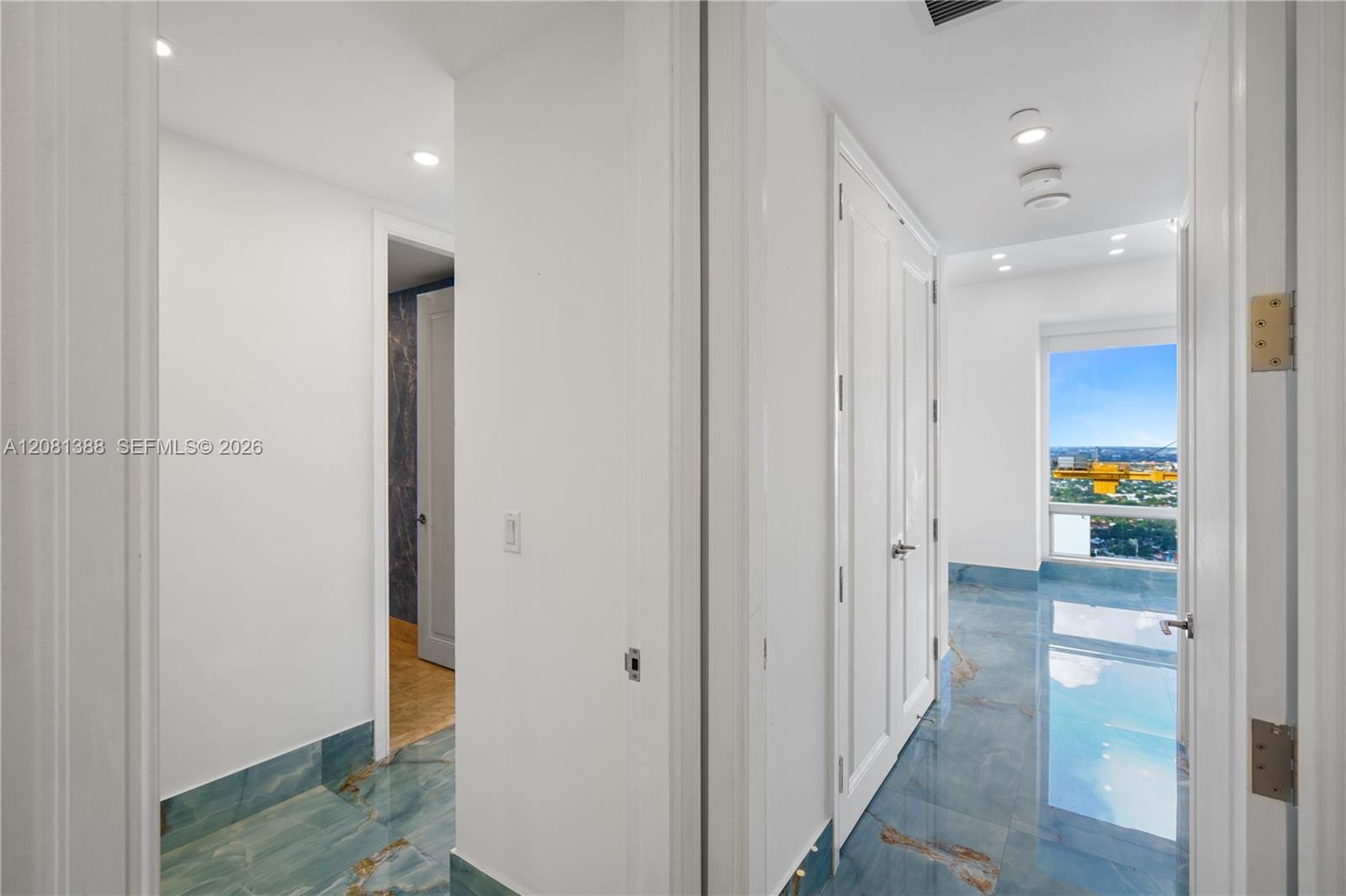 Hallway featuring polished blue-toned stone flooring, recessed ceiling lighting, and full-height interior doors